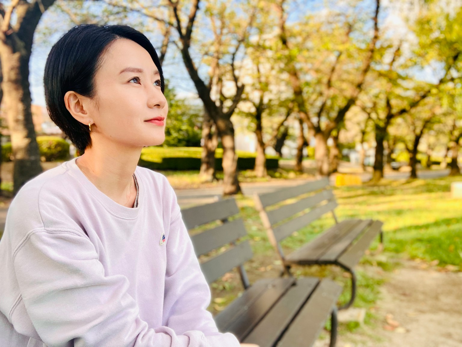 หญิงสาวนั่งอยู่บนม้านั่งในสวนมองไปอย่างมีความคิด