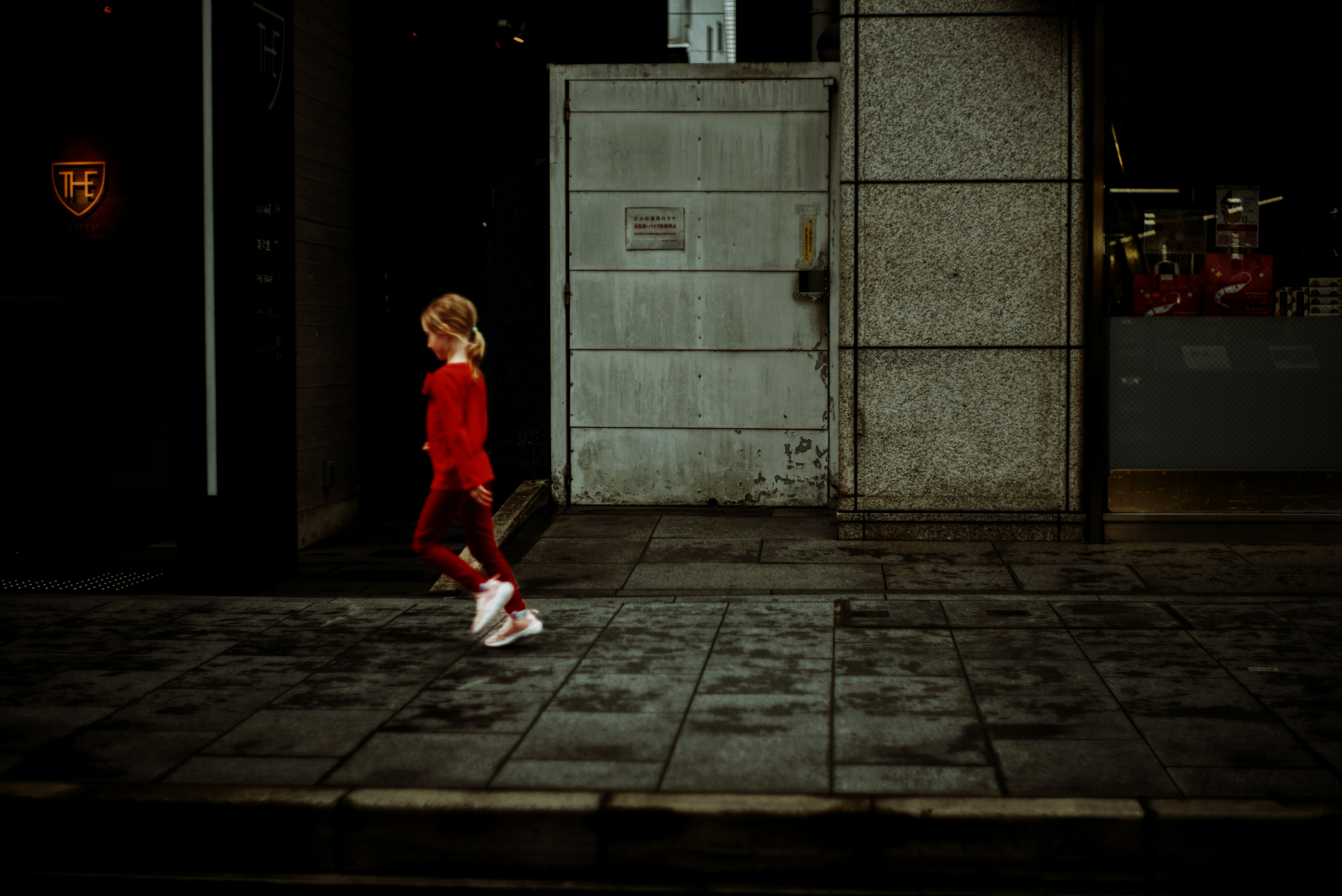 路地の壁際を歩く赤い服の人物