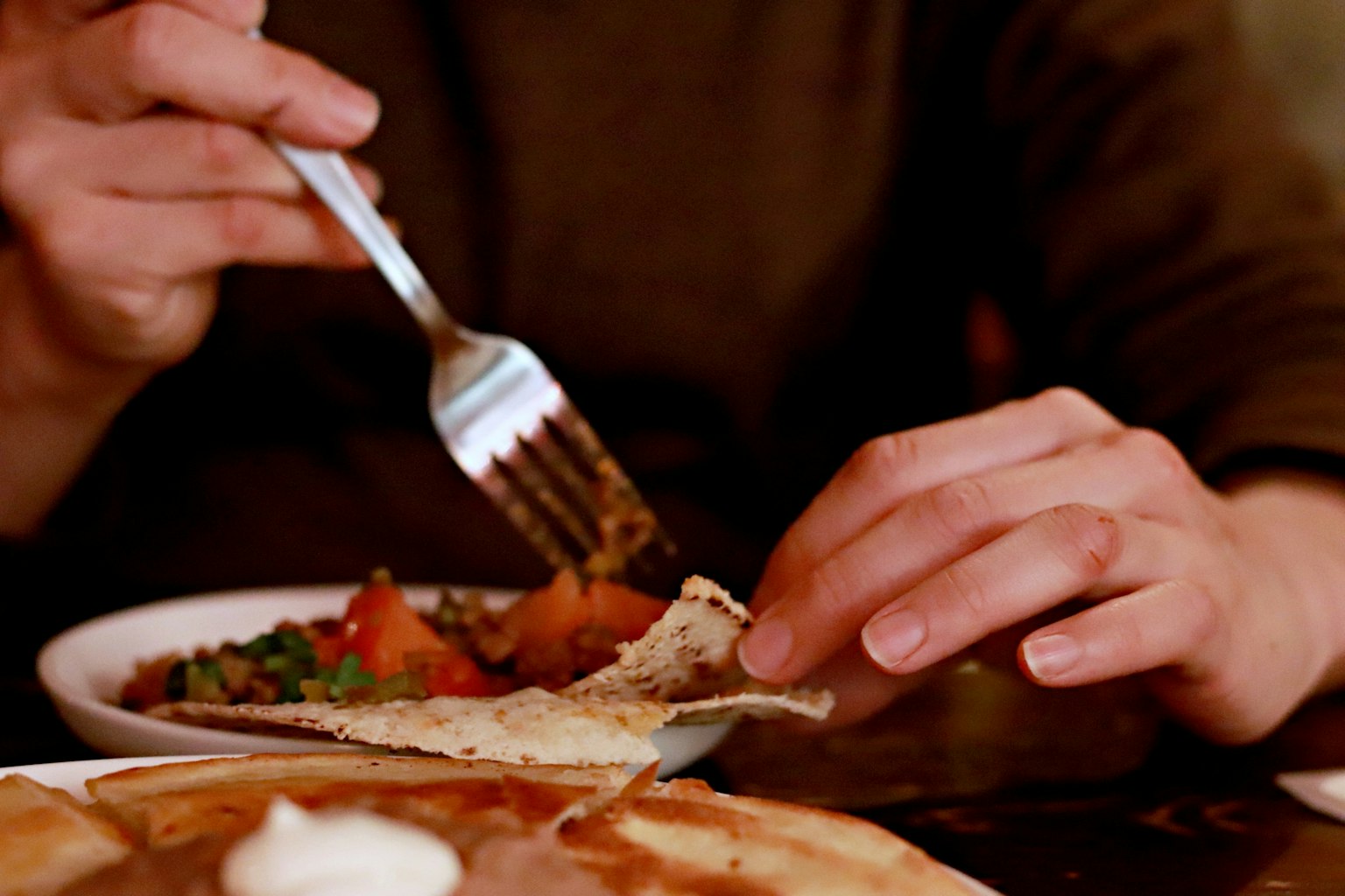 La mano di una persona che usa una forchetta per prendere cibo da un piatto