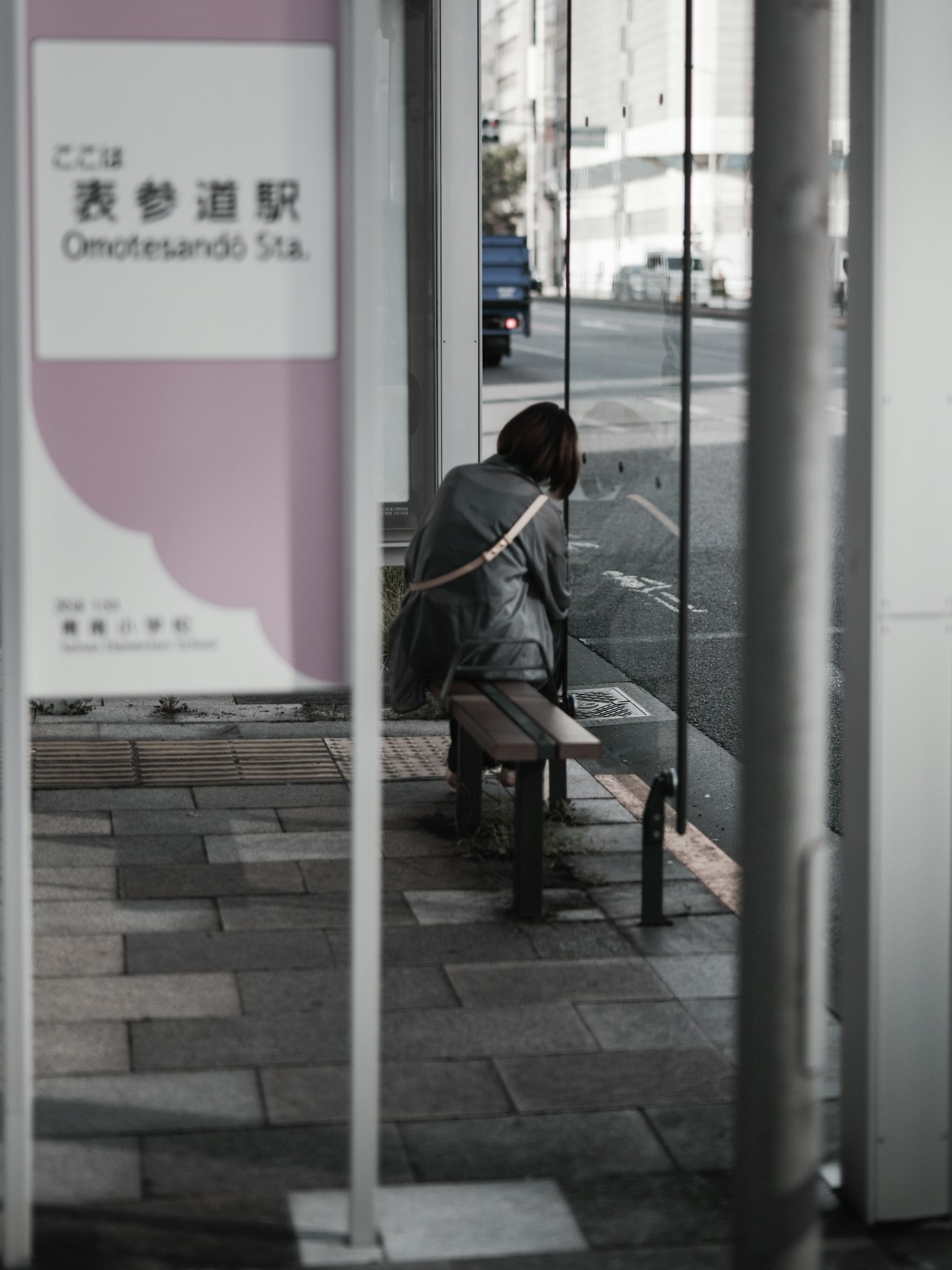 Woman sitting at a bus stop with a station sign
