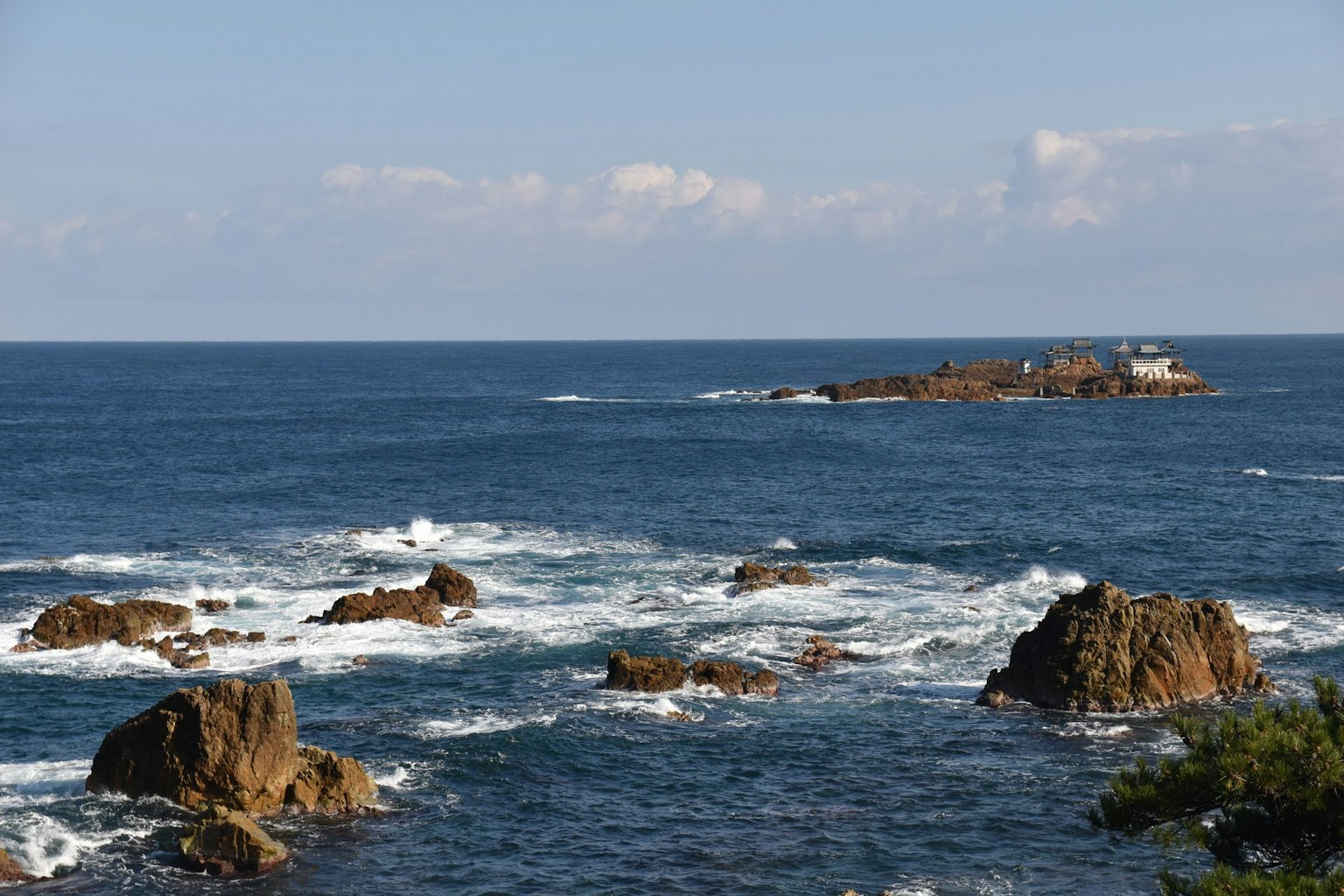 Vista escénica del océano azul con costa rocosa y una pequeña isla a lo lejos