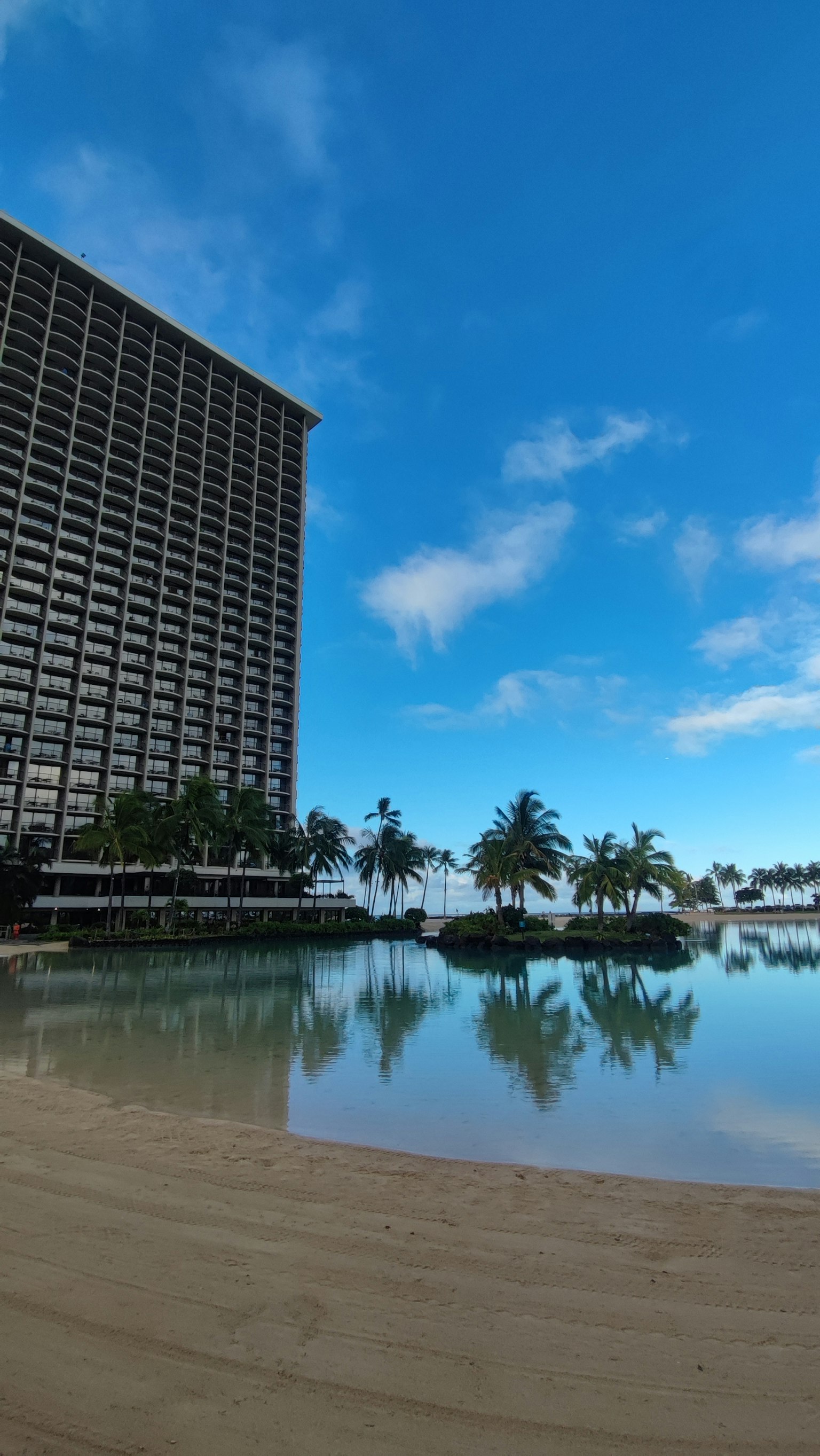 Strandansicht mit einem Resort-Hotel, das sich im Wasser spiegelt und einem klaren blauen Himmel