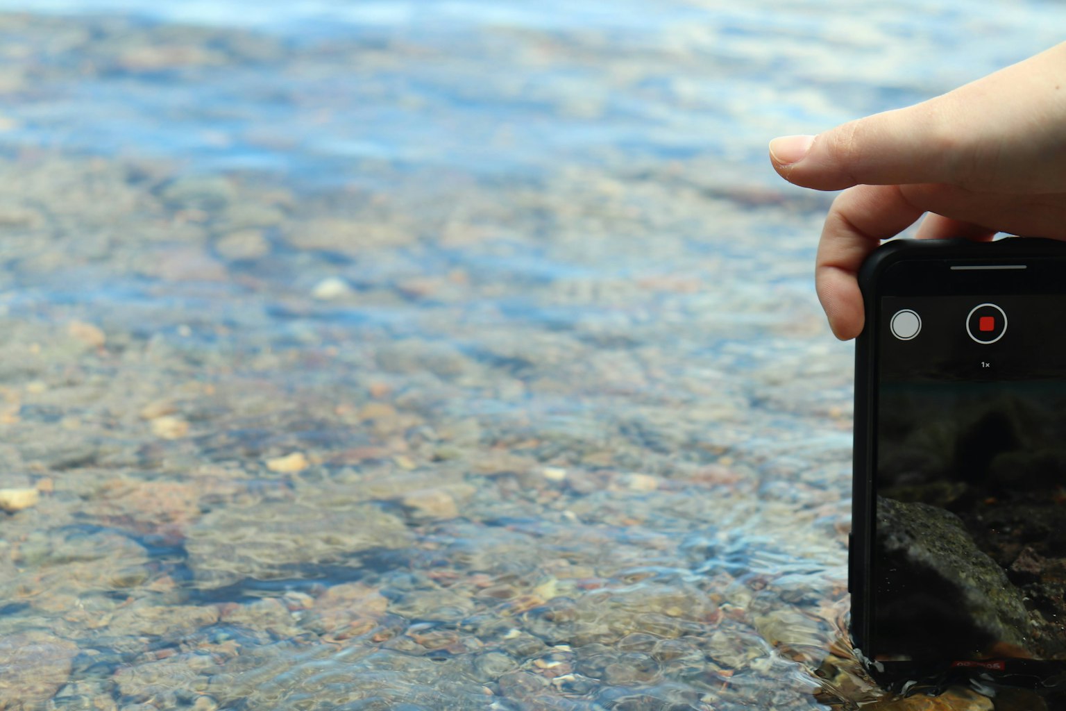 Mano che tiene uno smartphone vicino a una superficie d'acqua chiara