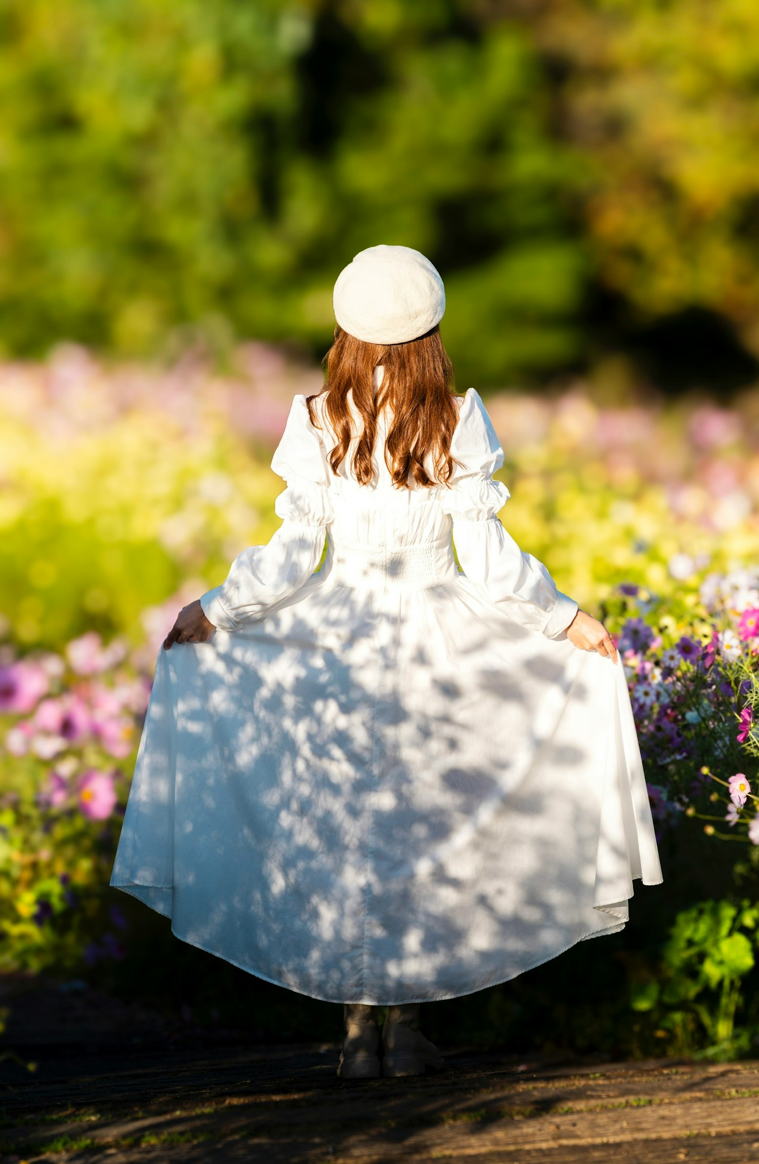 白いドレスを着た女性が花畑の中で後ろを向いている