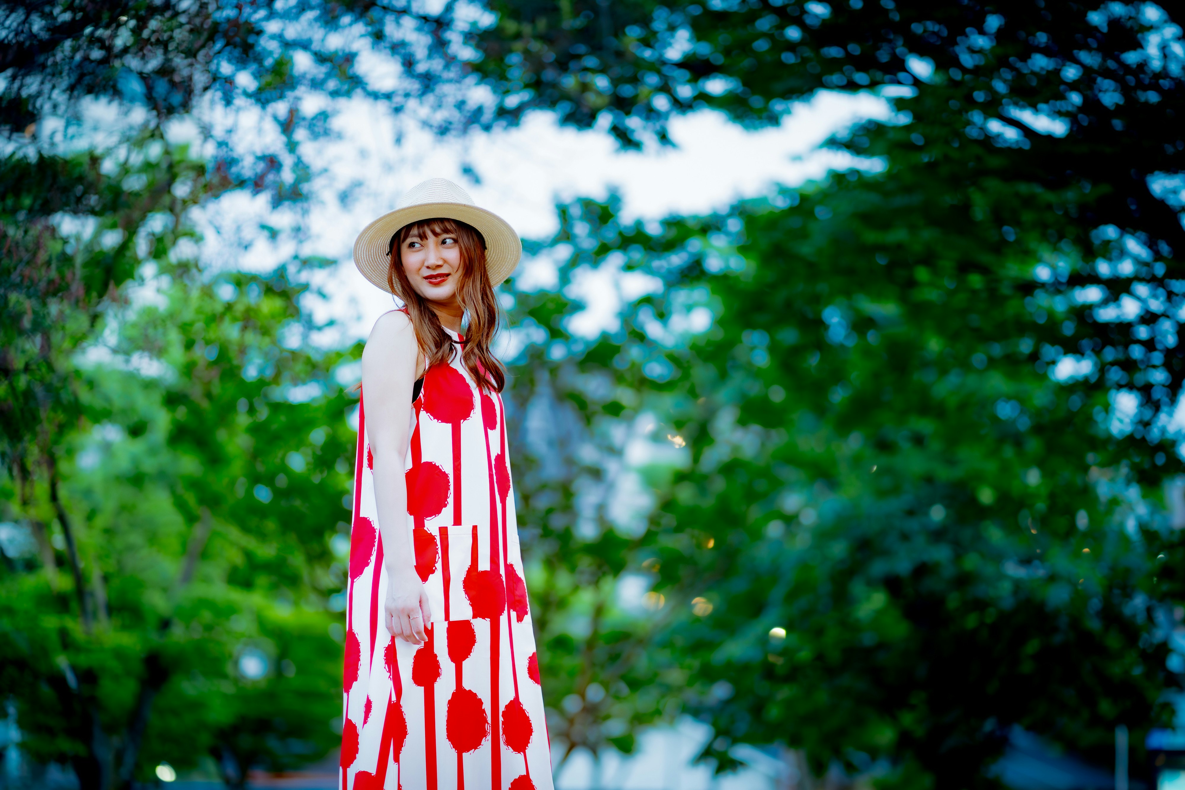 Woman standing outdoors in a red floral dress with lush green background