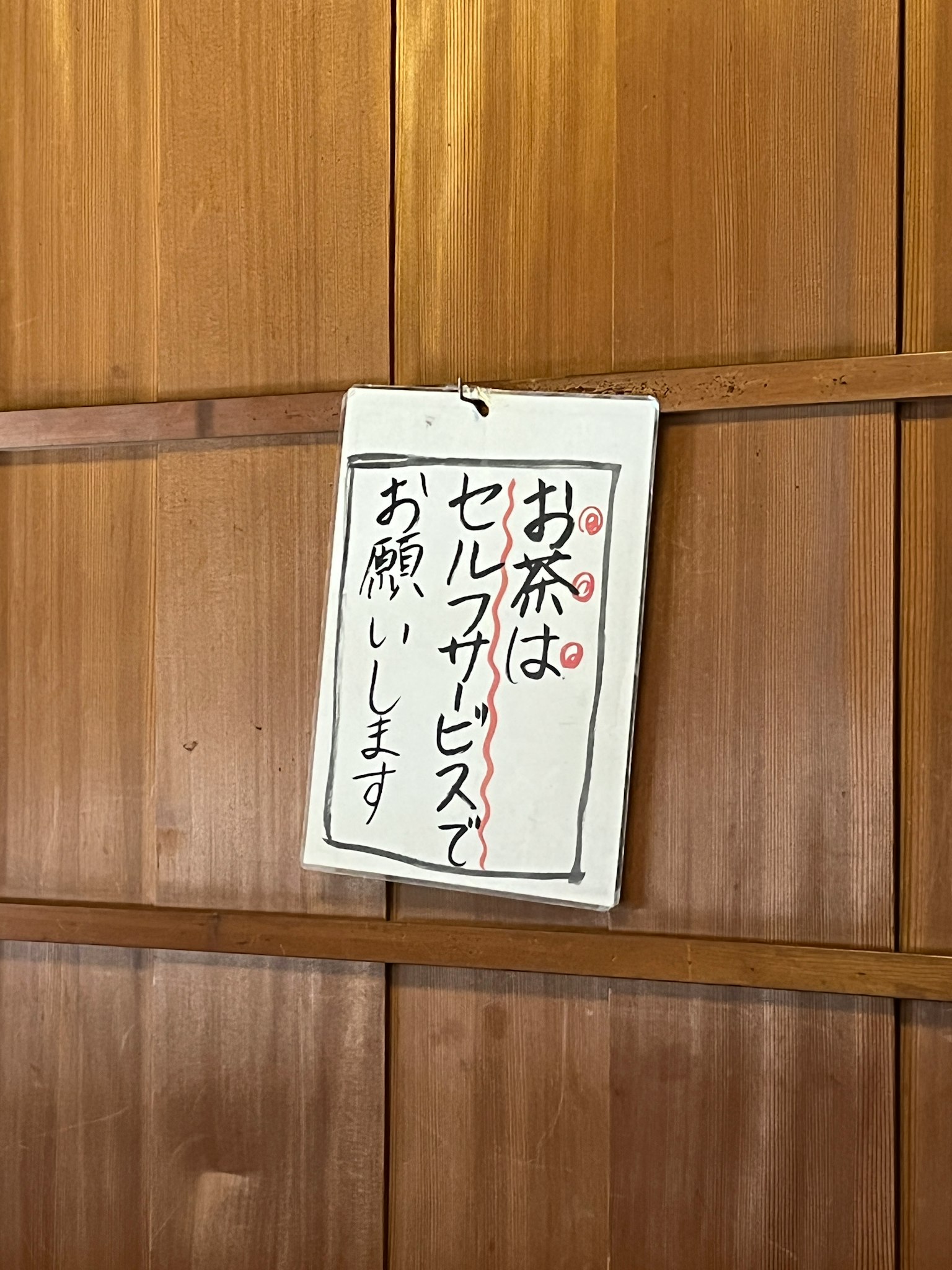 Schild für Selbstbedienungstee an einer Holzwand