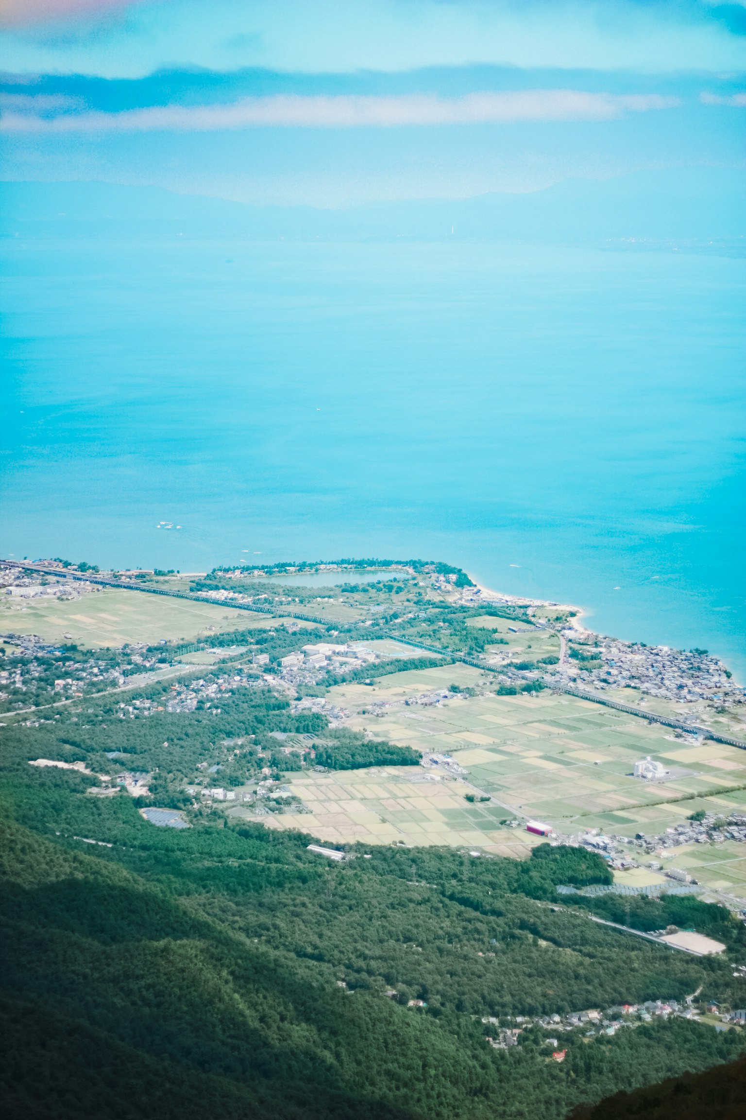 蓝色海洋和绿色山丘的鸟瞰图，海岸定居点在晴朗的天空下