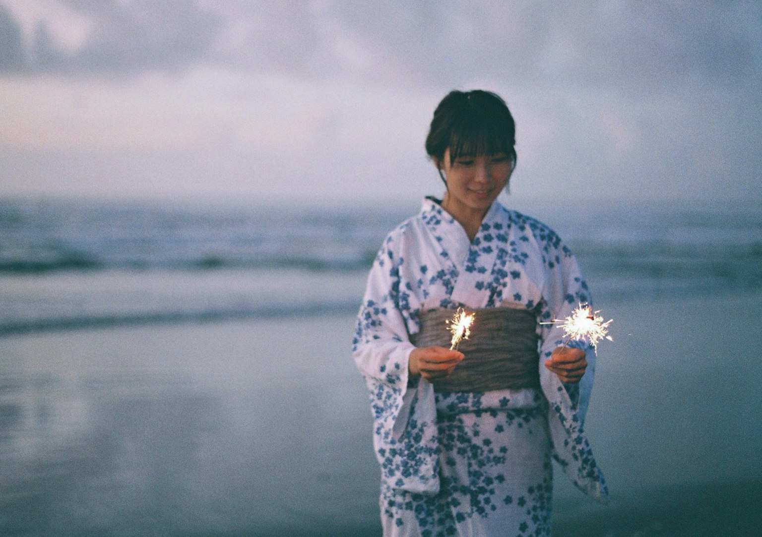 Donna in kimono che tiene dei fuochi d'artificio sulla spiaggia