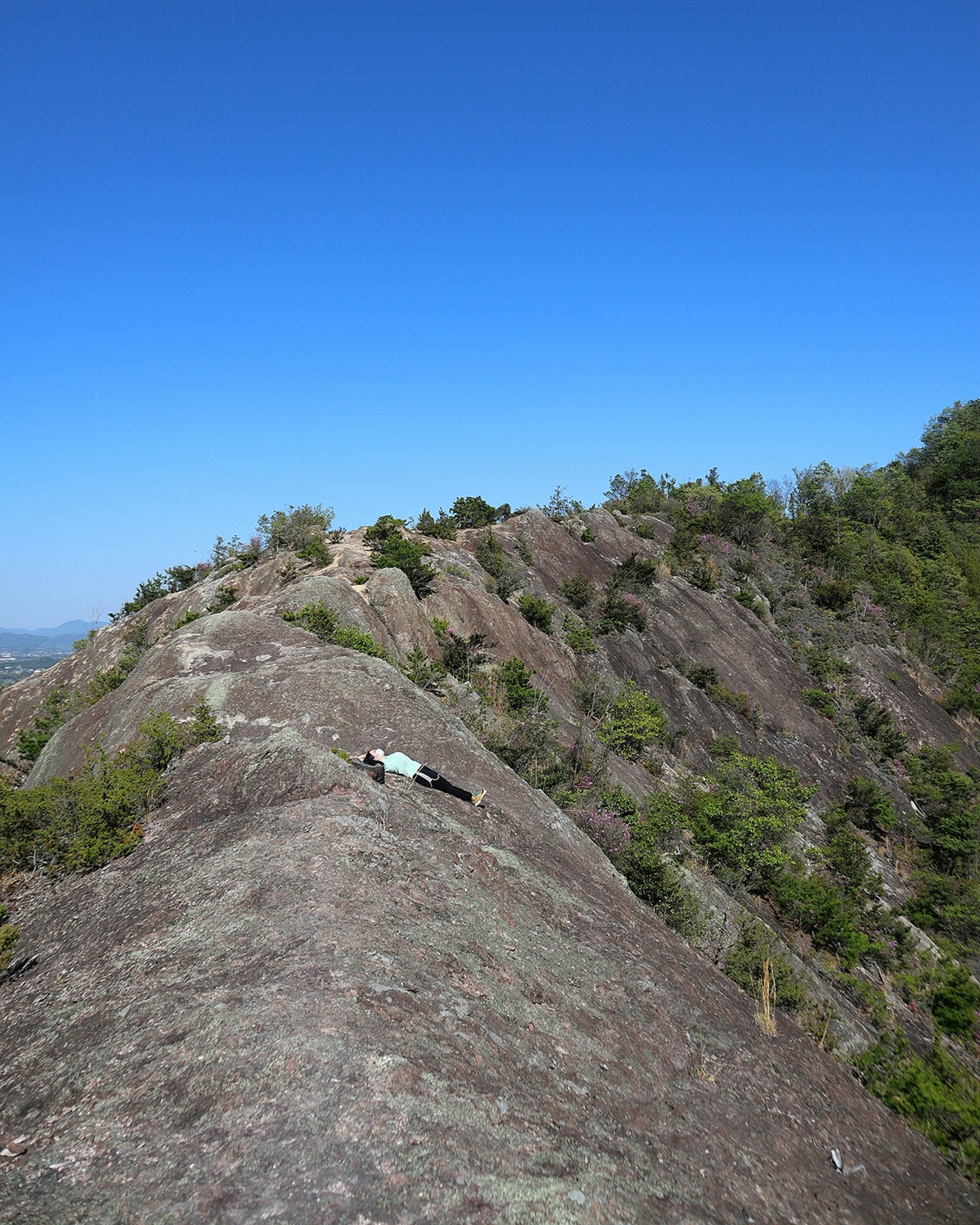 Person lying on a mountain ridge with clear blue sky