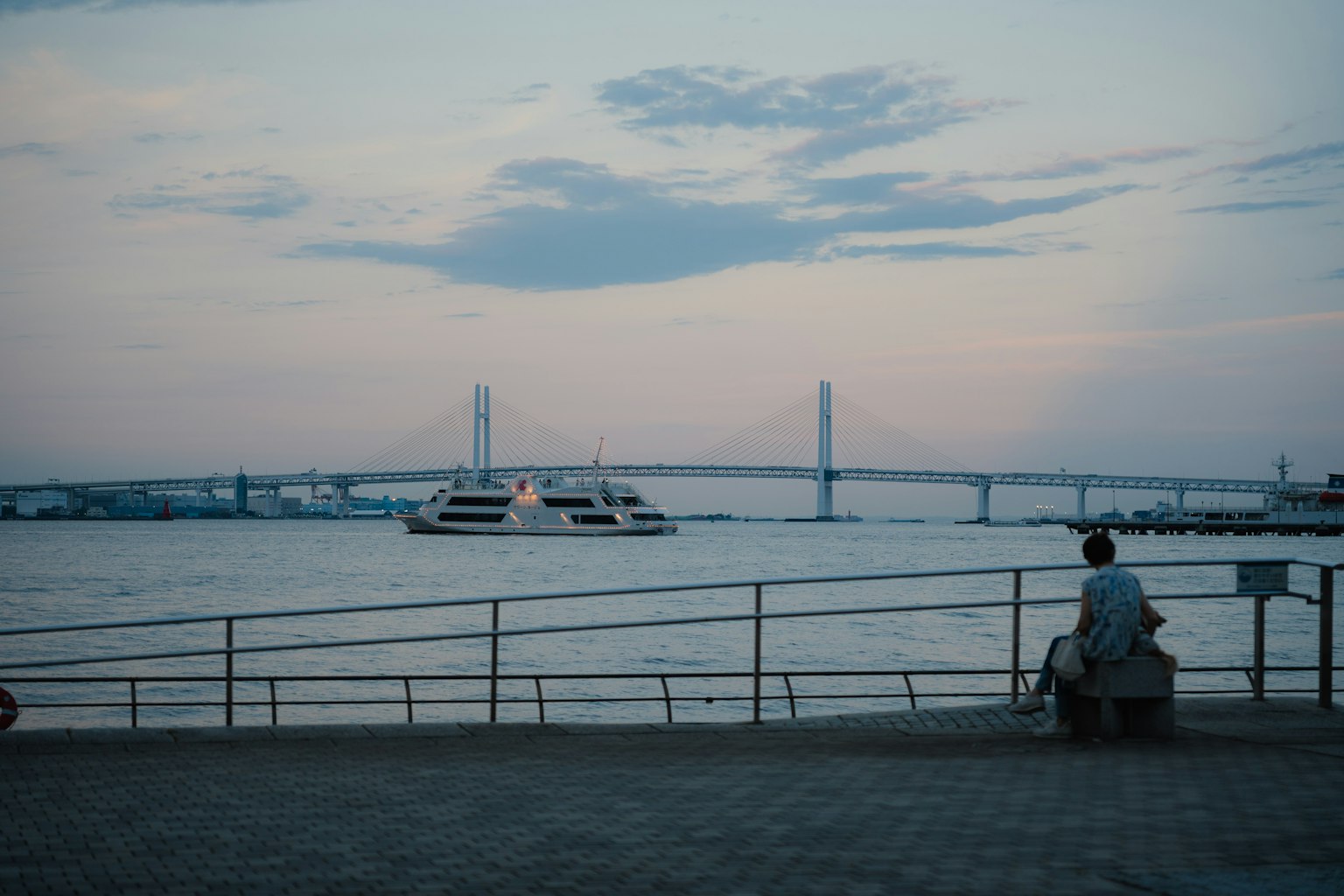 Personne assise au bord de l'eau au crépuscule avec un pont en arrière-plan
