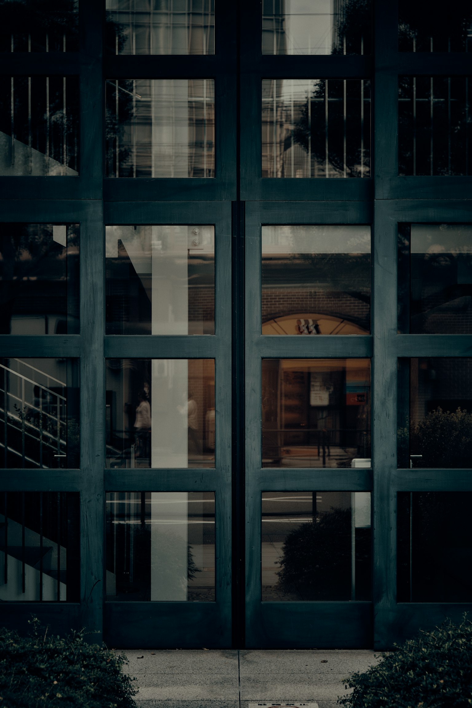 Entrée d'un bâtiment moderne avec des portes en verre vert foncé et un intérieur visible