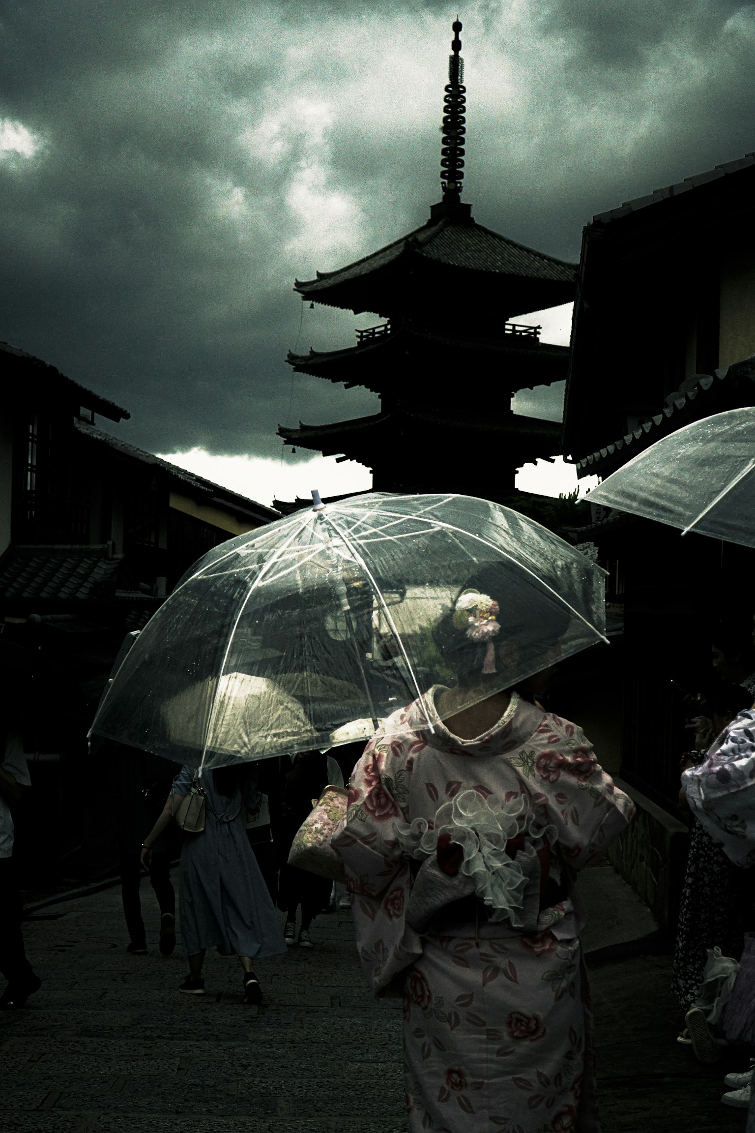 Frau im Kimono mit transparentem Regenschirm unter einem dunklen Himmel mit einer traditionellen Pagode