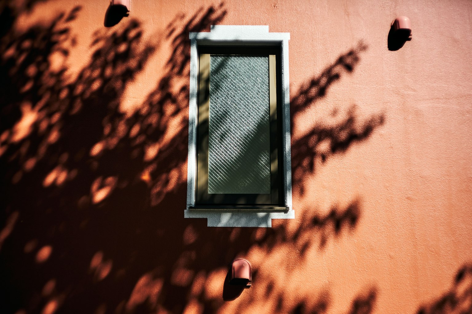 Una finestra su un muro arancione con interessanti motivi d'ombra