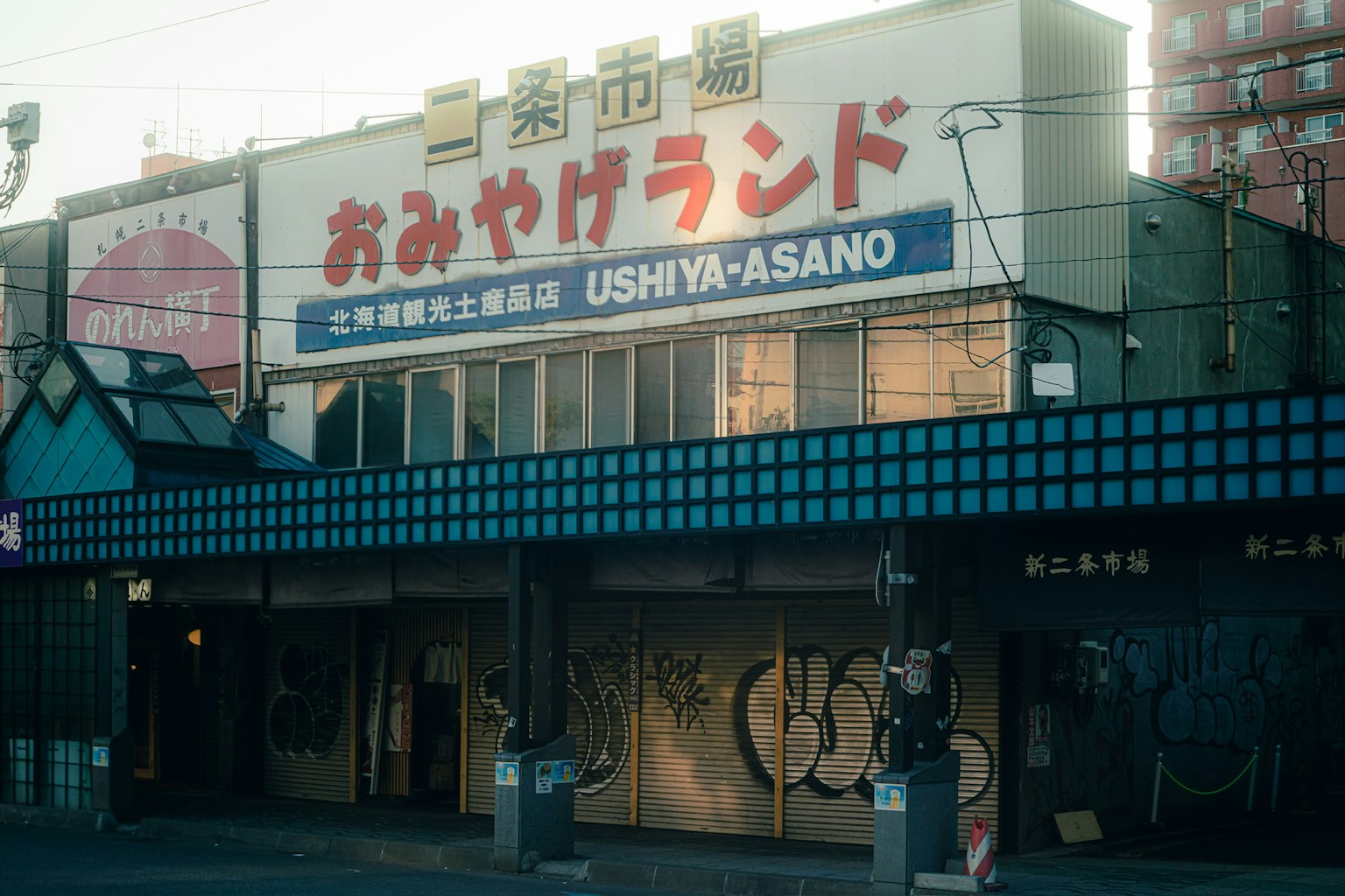 Extérieur d'un ancien bâtiment commercial avec l'enseigne OMIYA LAND et le nom USHIYA-ASANO