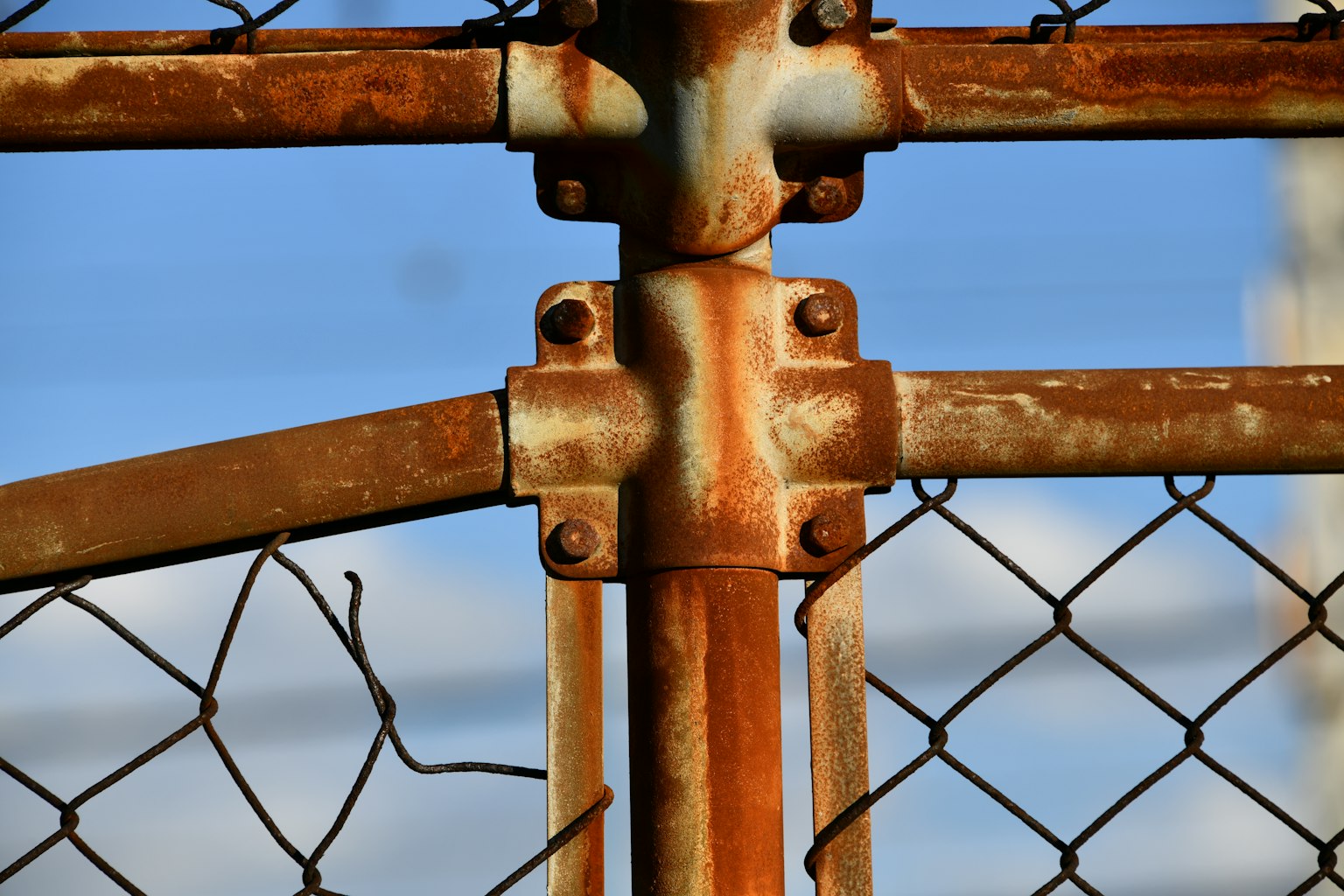 Nahaufnahme eines rostigen Metallzauns vor blauem Himmel