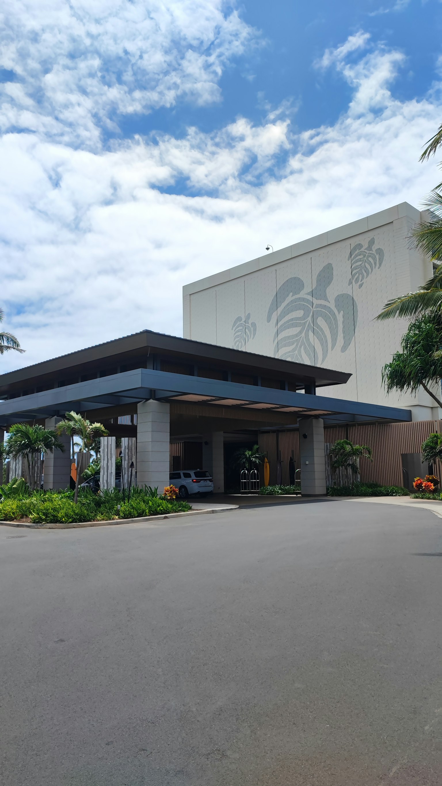 Extérieur moderne d'un hôtel avec entrée entourée de verdure sous un ciel bleu et des nuages