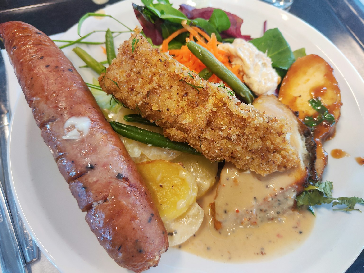 Un plato con pollo empanizado crujiente y salchicha acompañado de verduras frescas y salsa gravy