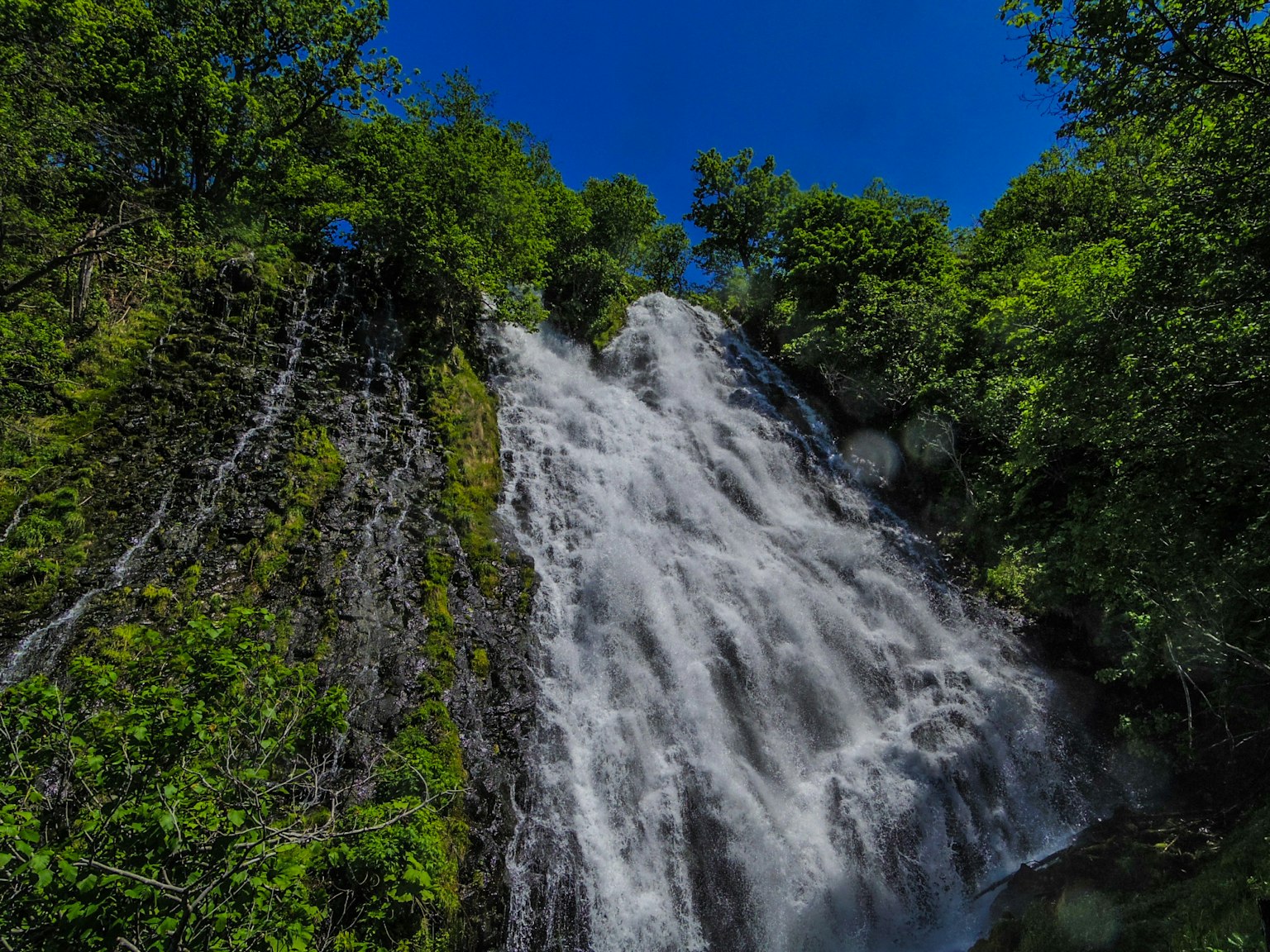 Beautiful waterfall flowing under a blue sky surrounded by green trees