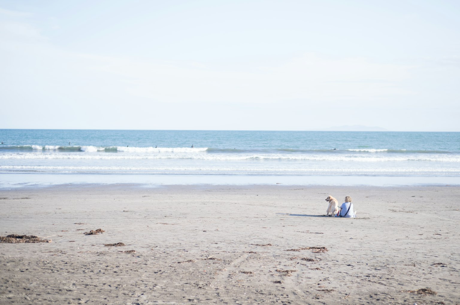 Zwei Personen sitzen an einem Strand mit sanften Wellen und klarem Himmel