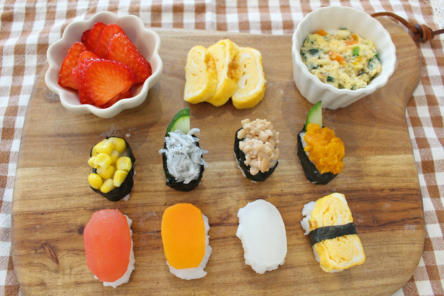 ซูชิสีสันสดใสจัดเรียงบนไม้กับสตรอว์เบอร์รีและข้างเคียง