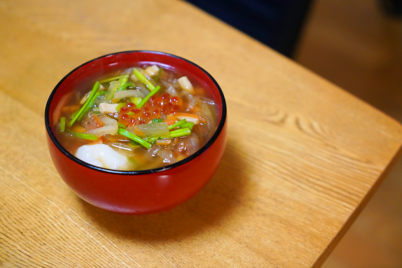 一碗豐富的湯裝在紅色碗中，上面點綴著切碎的蔥