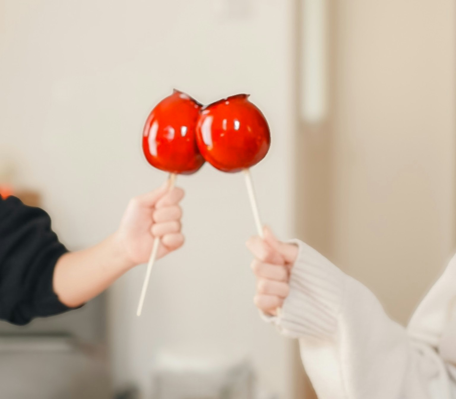 赤いリンゴ飴を持つ二人の手が向かい合っている