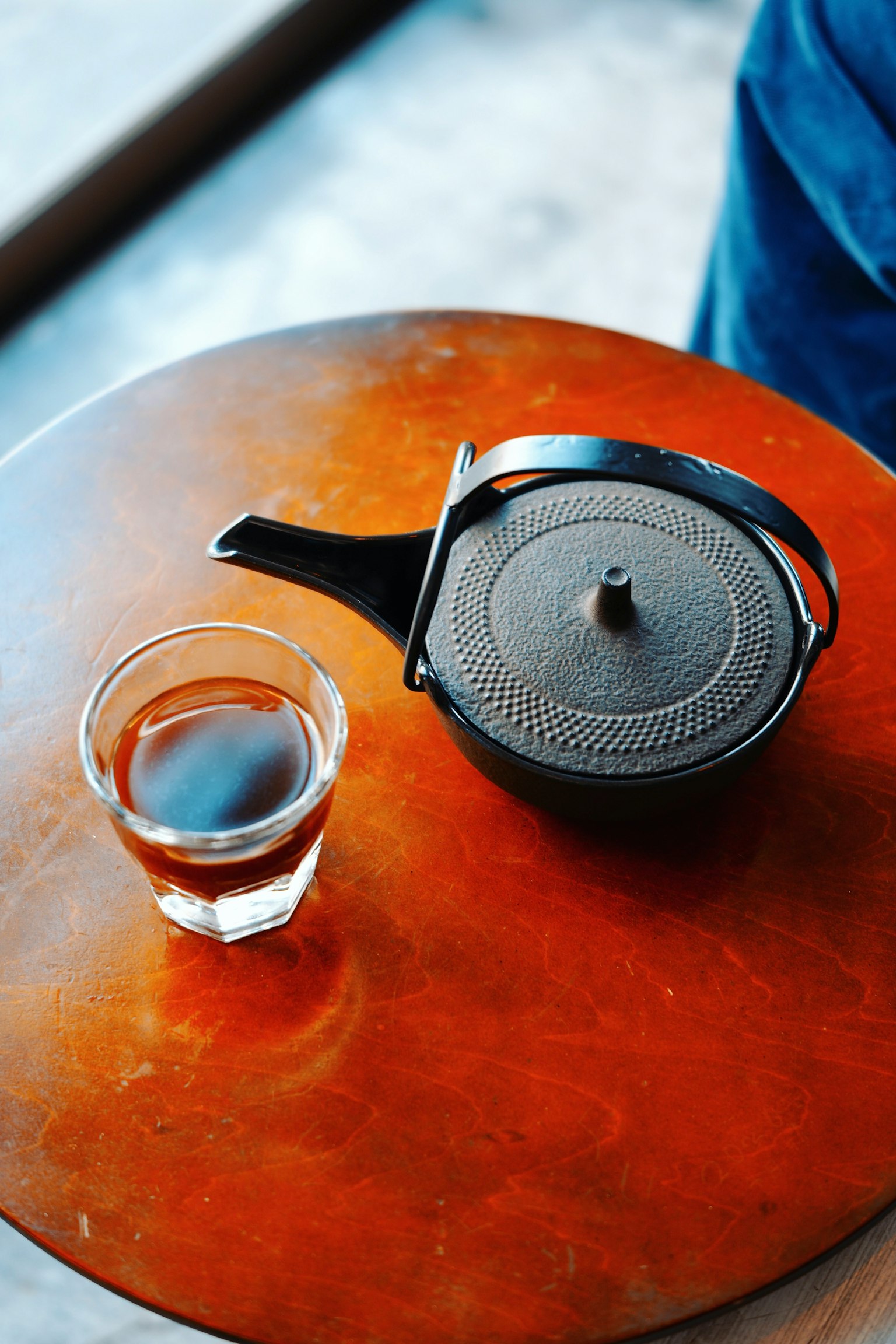 Black teapot and transparent glass of tea on a wooden table