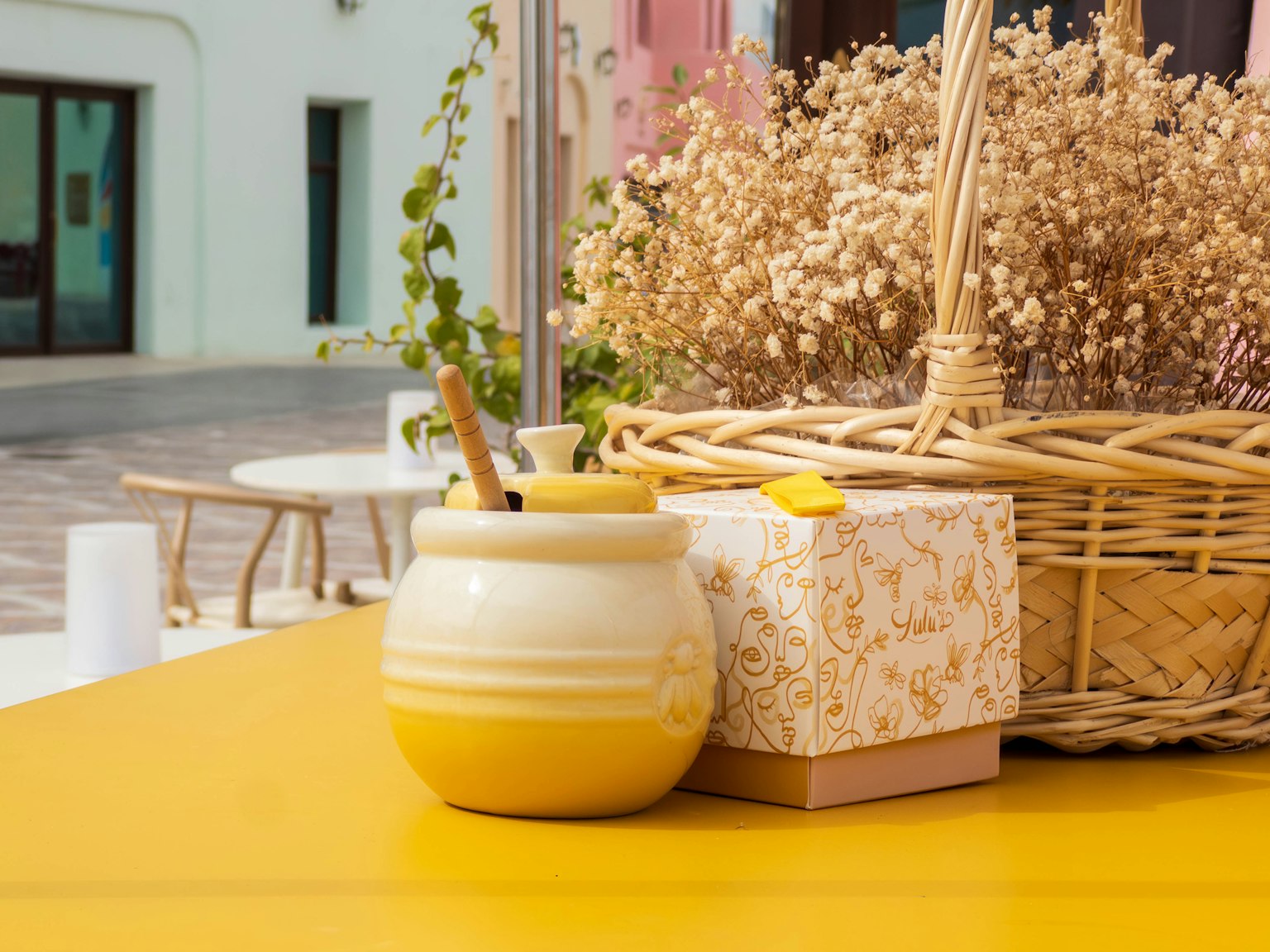 Un petit vase et une boîte sur une table jaune avec un panier de fleurs séchées