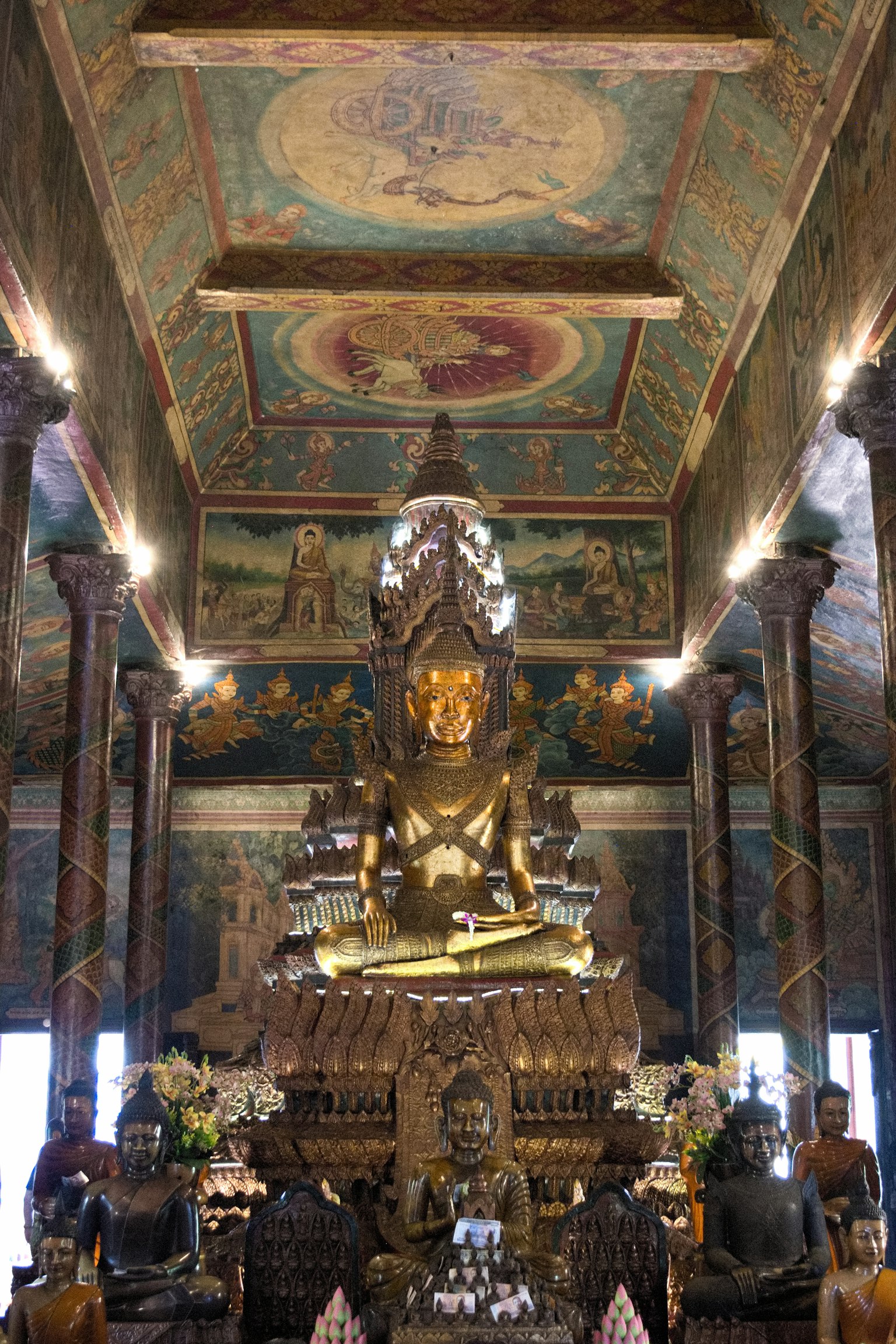 Interior de un templo con una gran estatua de Buda dorada rodeada de murales intrincados en las paredes y el techo