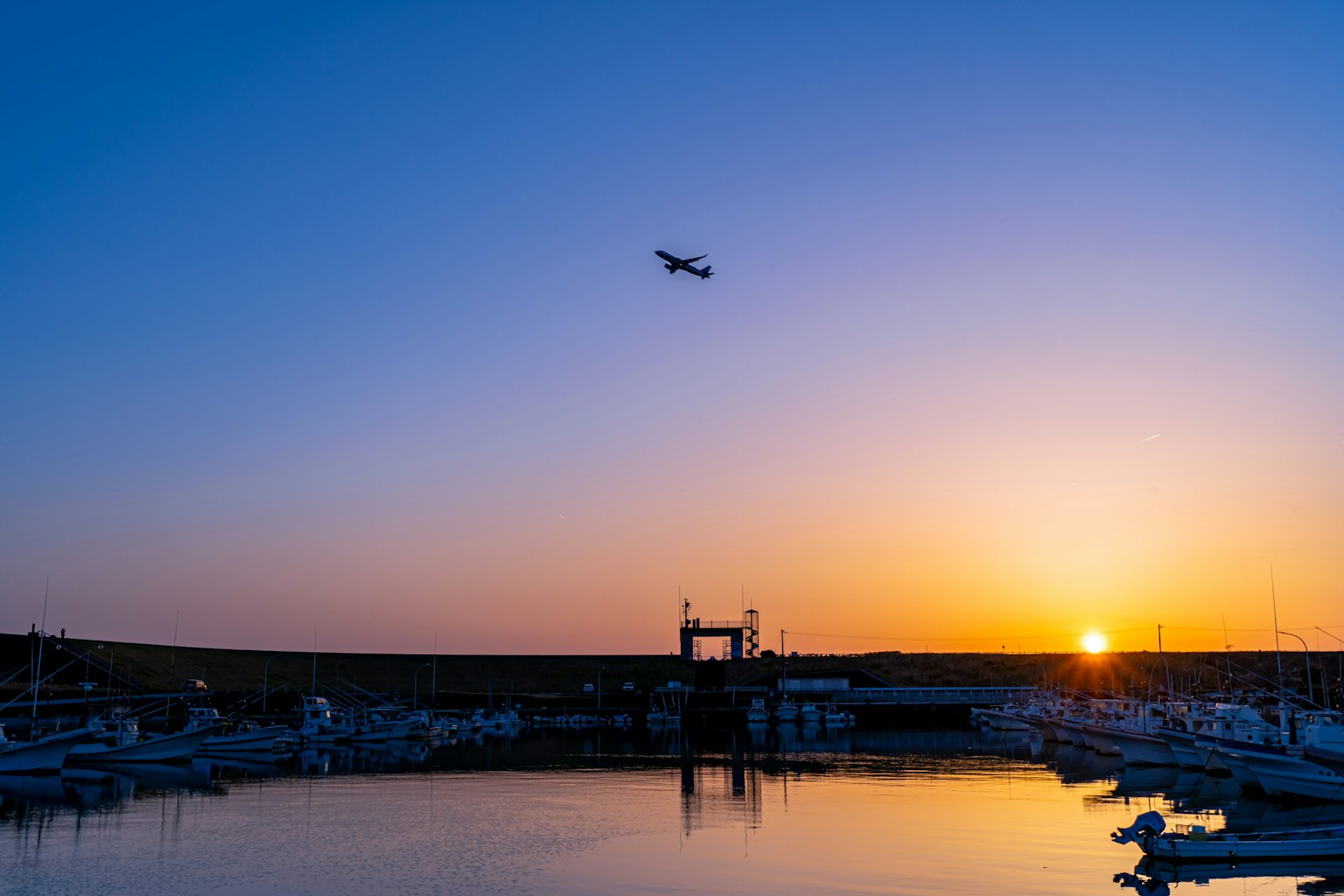 Ein Flugzeug fliegt über einen Hafen bei Sonnenuntergang mit ruhigen Wasserreflexionen