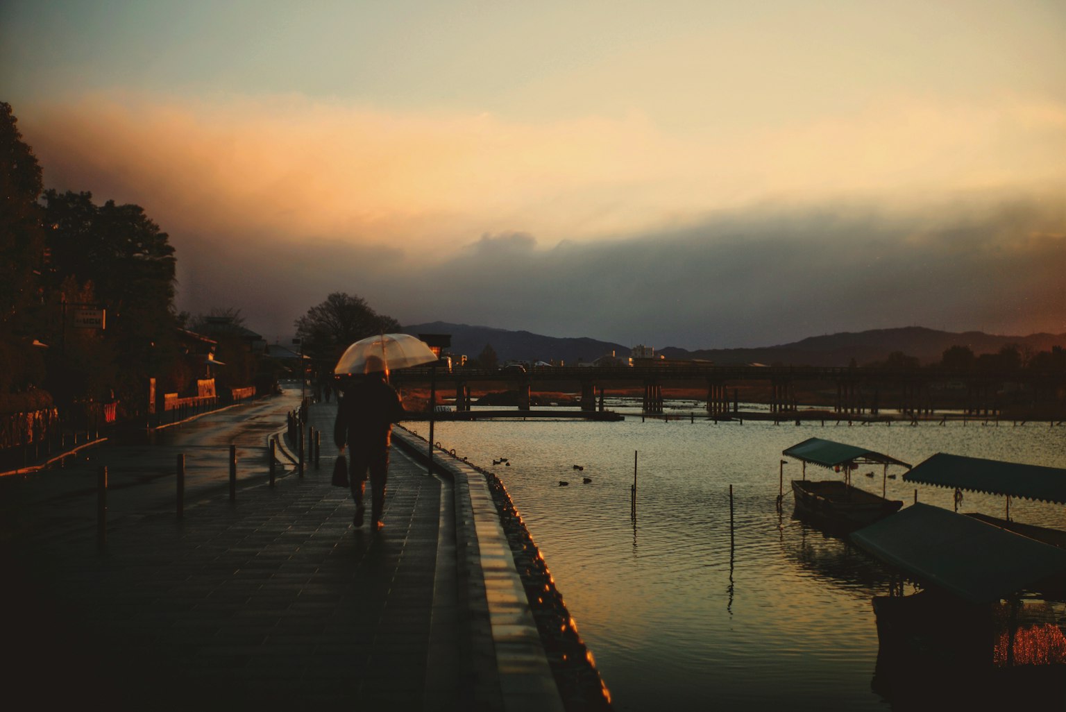 Personas caminando por un sendero junto al lago al atardecer con un paraguas