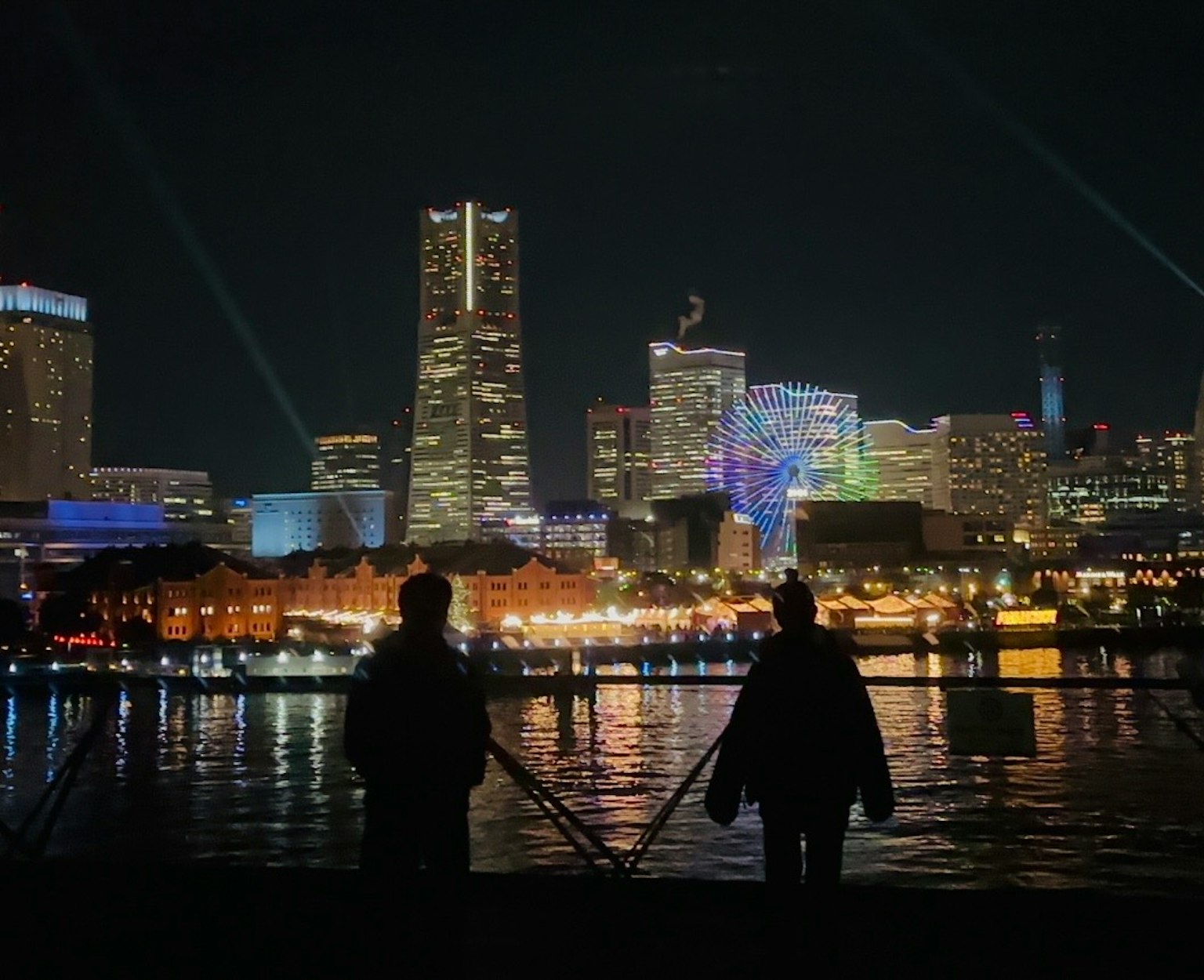 Silhouettes de deux personnes au bord de l'eau avec une skyline urbaine vibrante la nuit