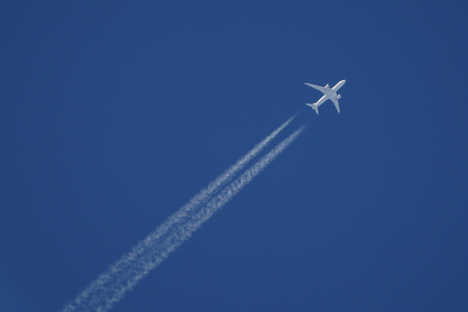 เครื่องบินบินอยู่ในท้องฟ้าสีฟ้าโดยทิ้งรอยทางสีขาว