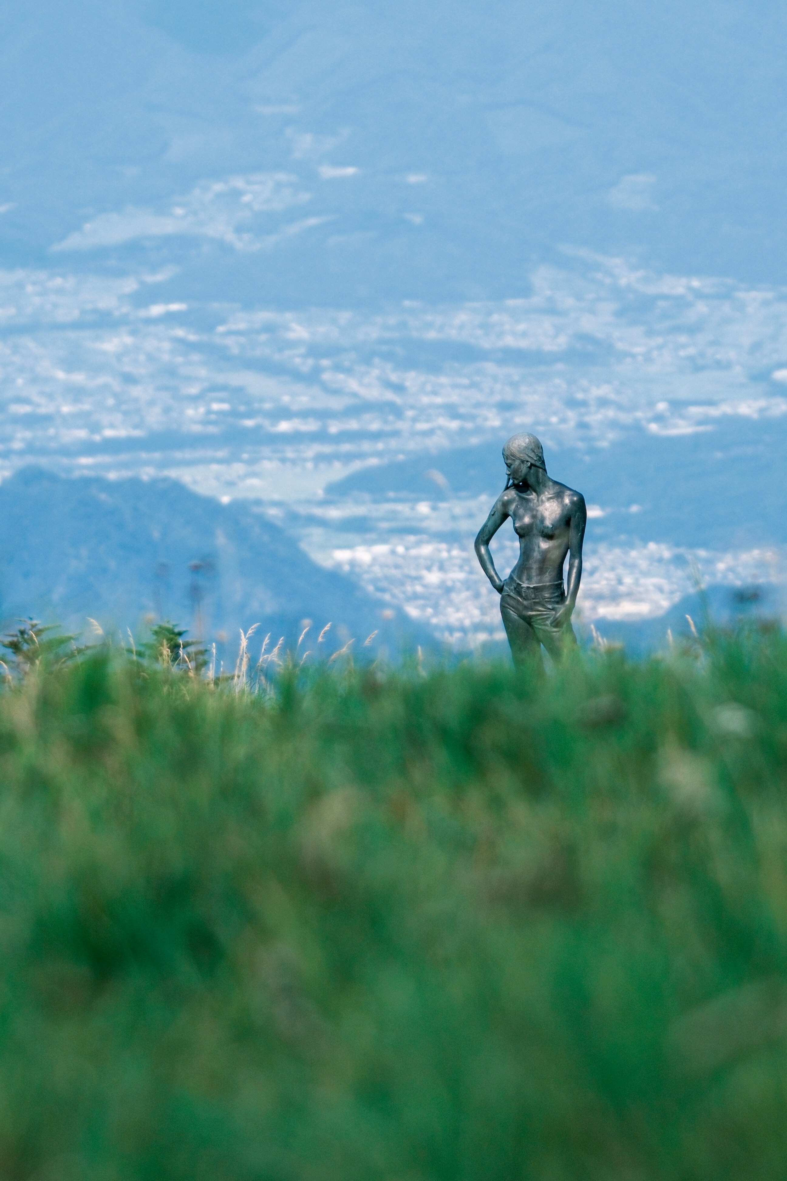 a statue-like figure standing in grass with mountain scenery