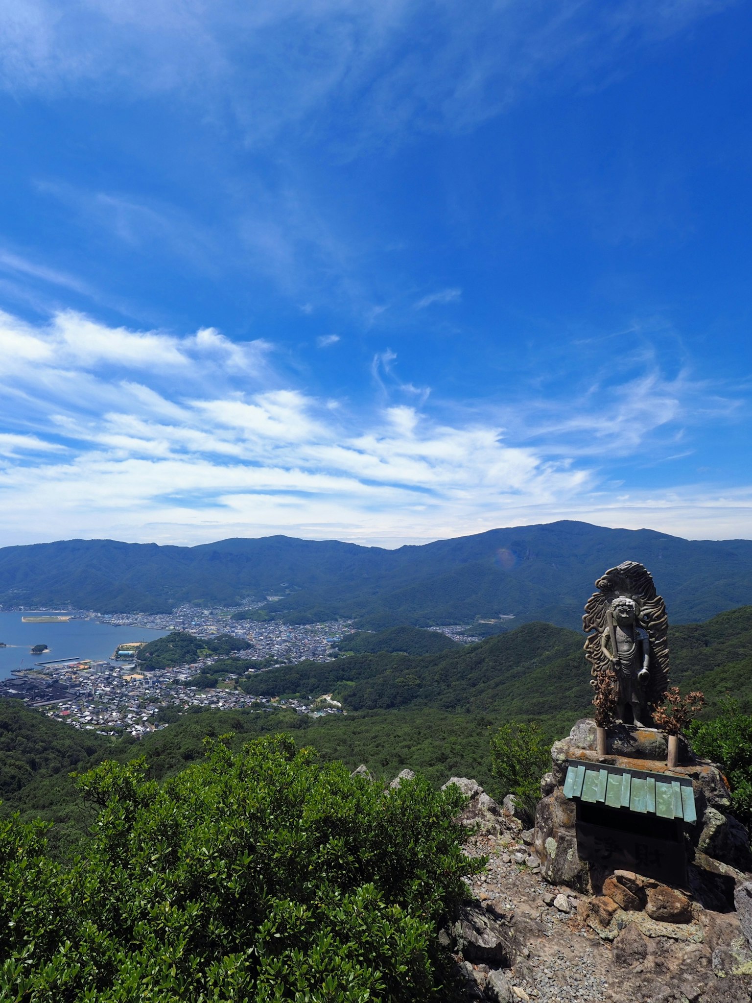 Panoramic view of mountains and town under blue sky with rock sculpture
