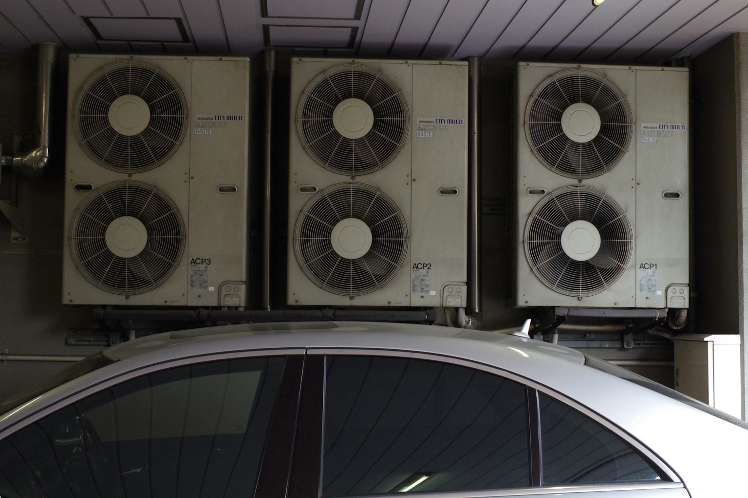 Cuatro unidades de aire acondicionado montadas en una pared junto a un coche plateado