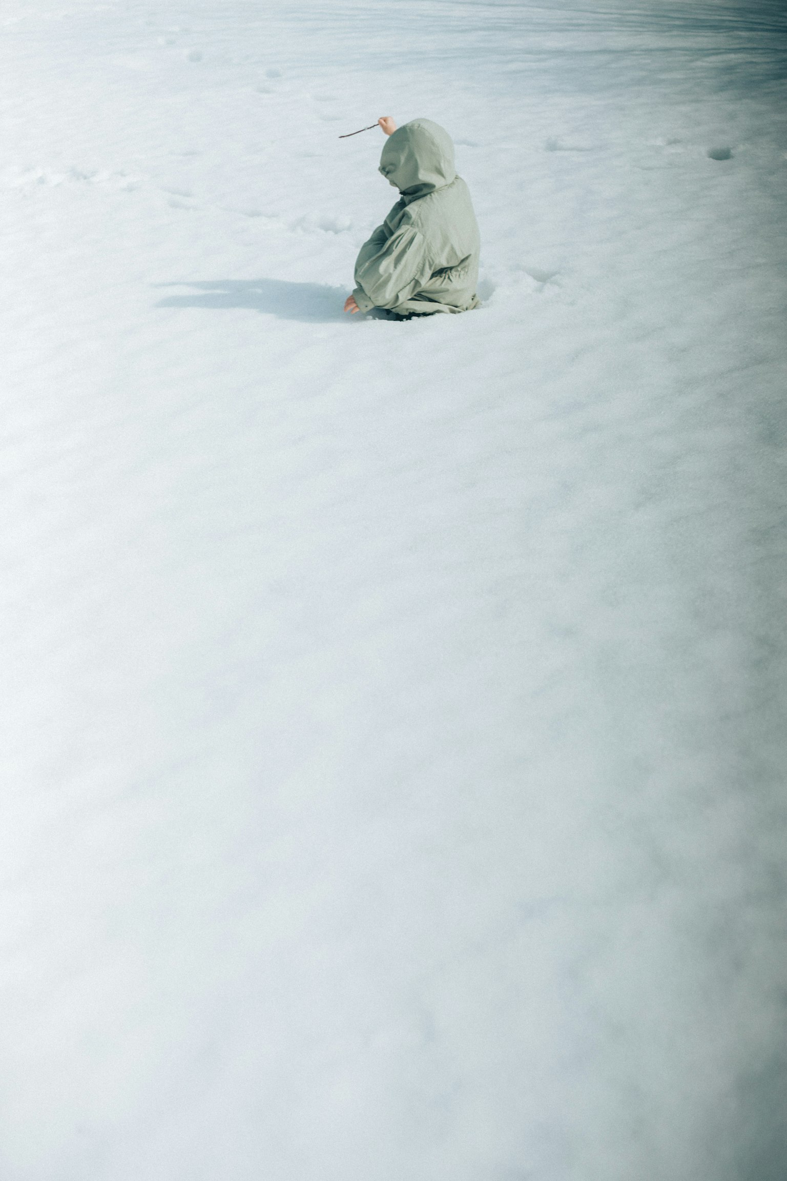 Niño sentado en la nieve con un abrigo verde claro