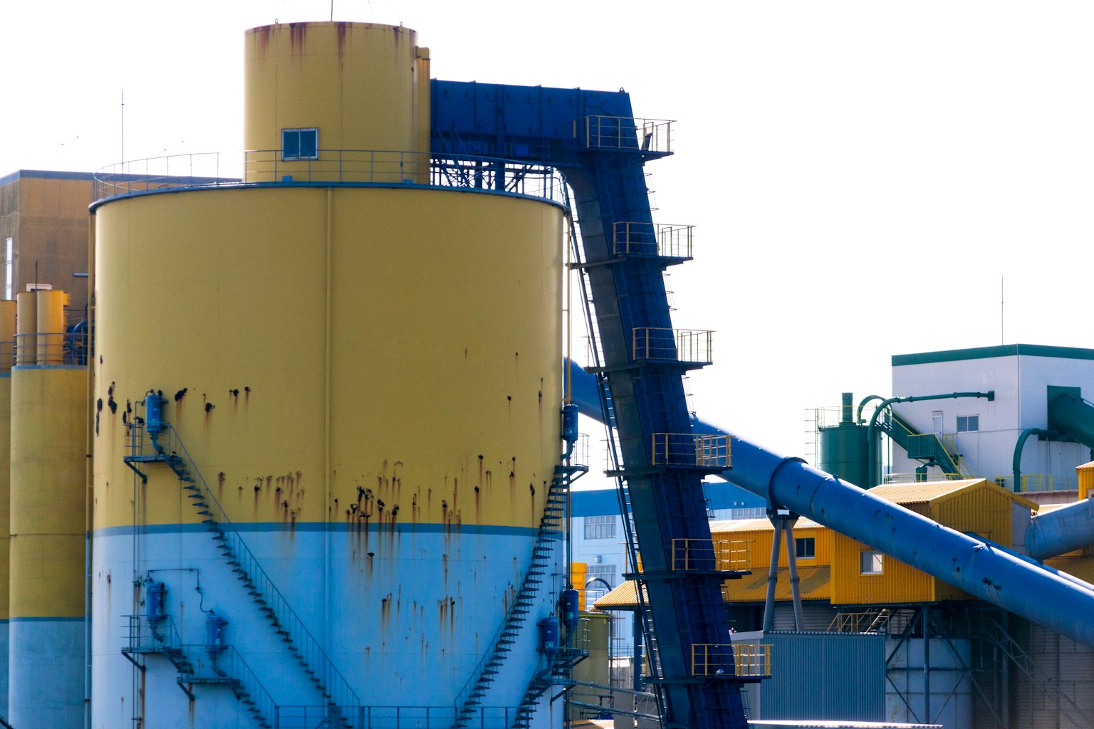 Large yellow and blue industrial tank with a conveyor belt at a factory
