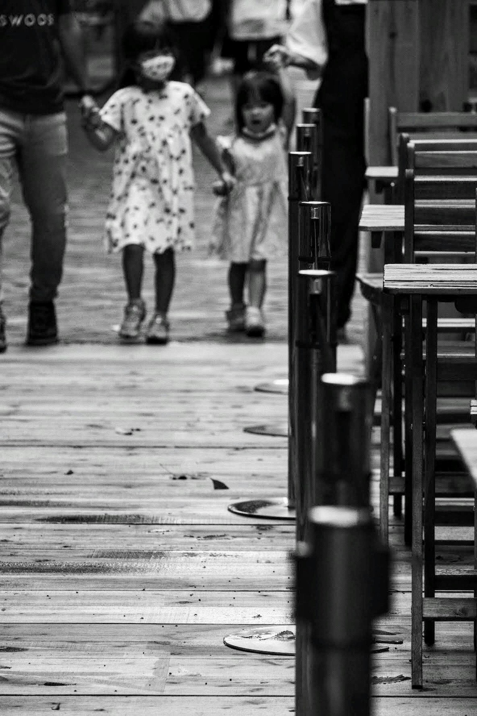 Dos niños tomados de la mano caminando por un camino de madera en blanco y negro