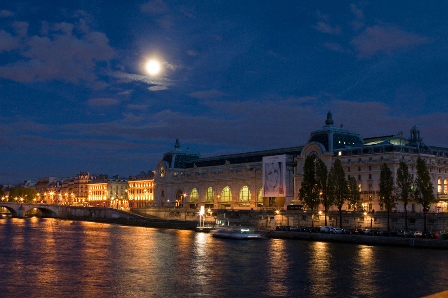 Night view of the Musée d'Orsay along the Seine River with a bright full moon