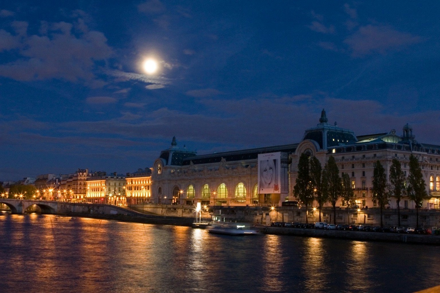 Vista nocturna del Museo de Orsay a lo largo del río Sena con una brillante luna llena