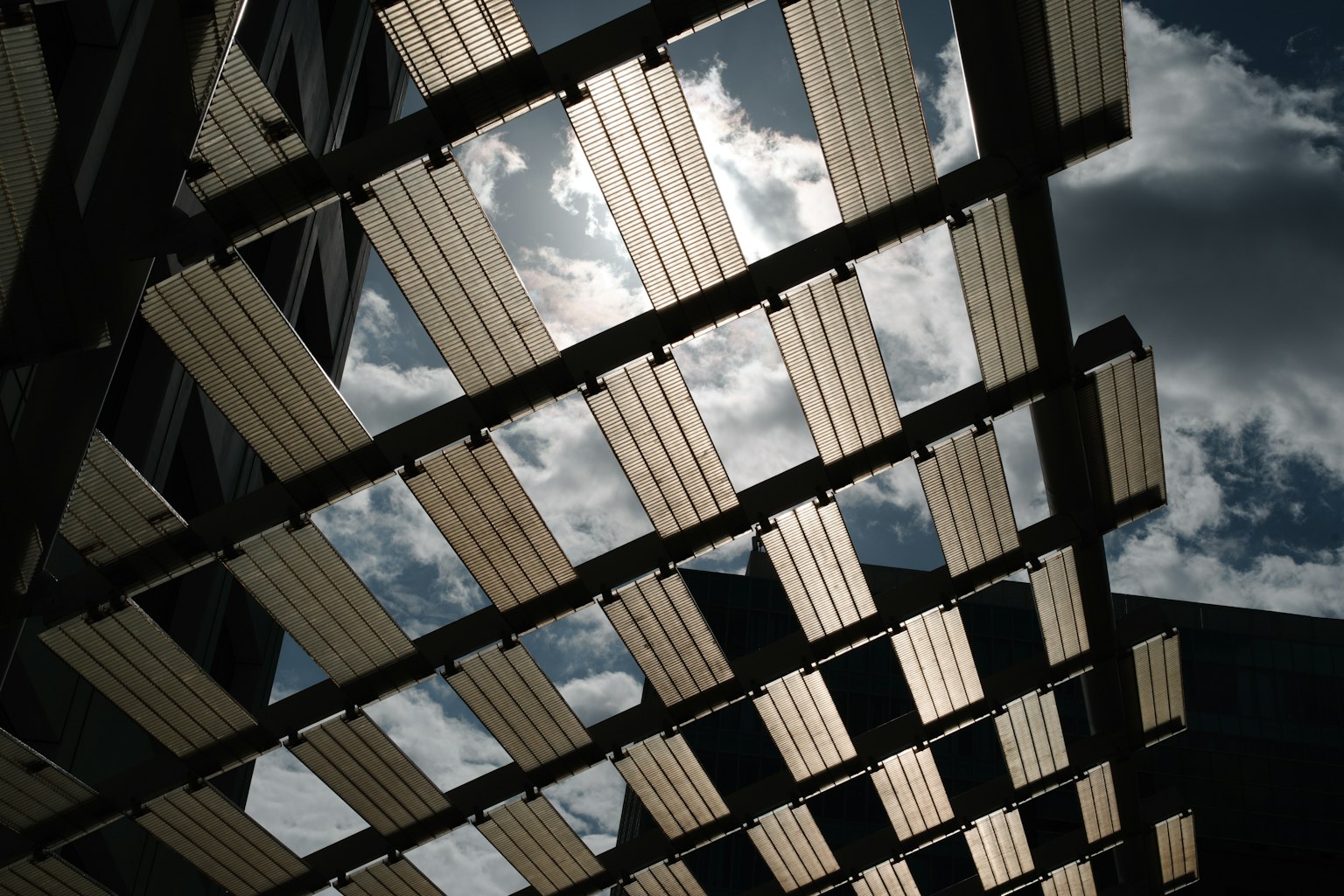 View of the sky from below a slatted structure sunlight filtering through clouds