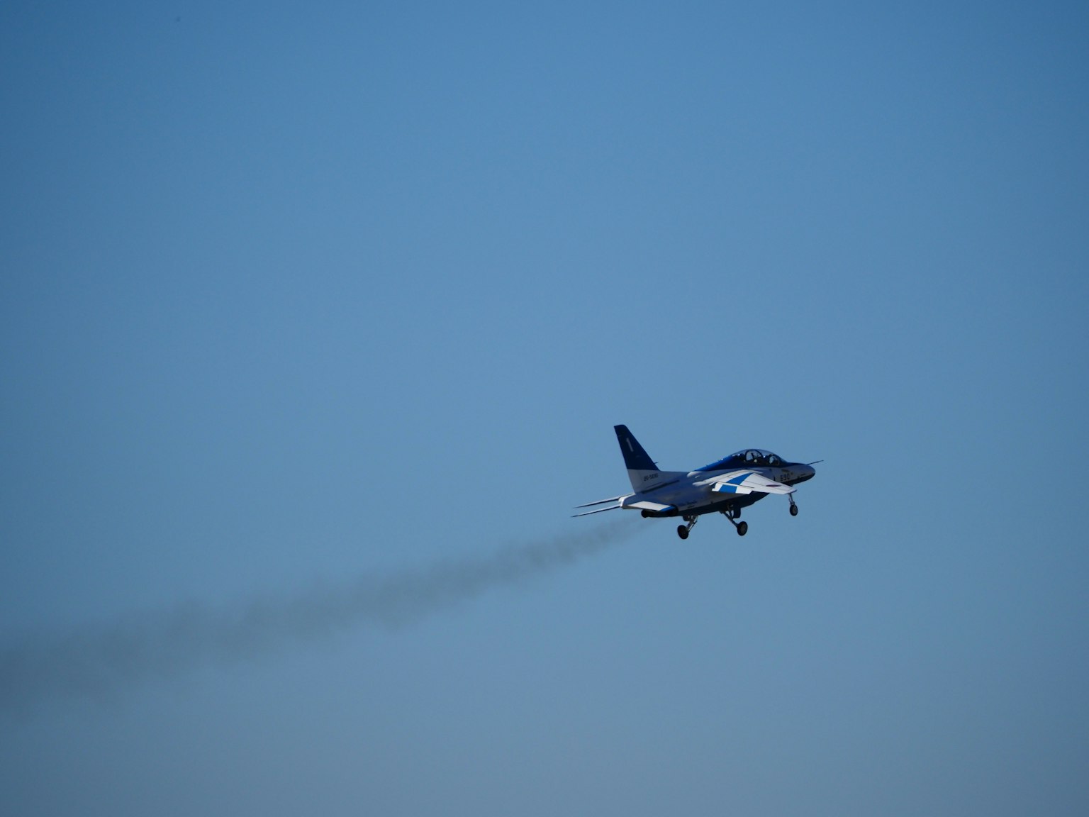 Un caza volando contra un cielo azul dejando una estela de humo