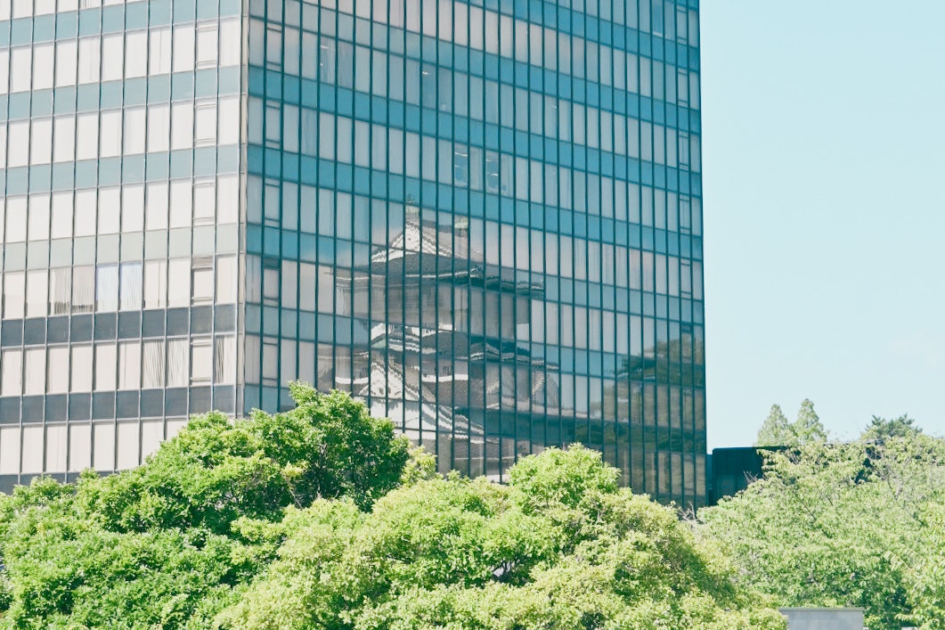 ガラス張りのオフィスビルと緑の木々のある街並み