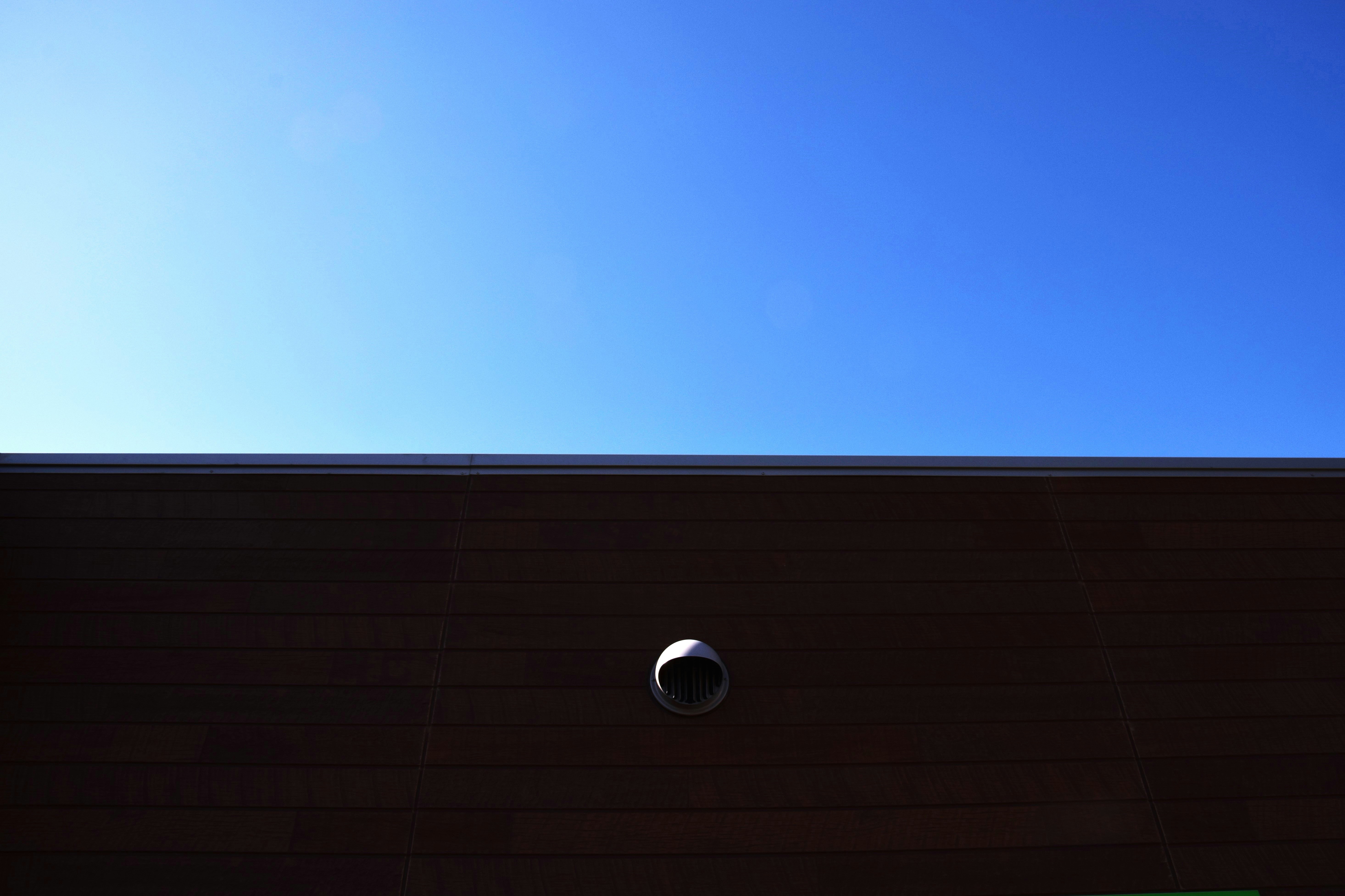 青空の下の建物の軒先と小さな丸い換気口