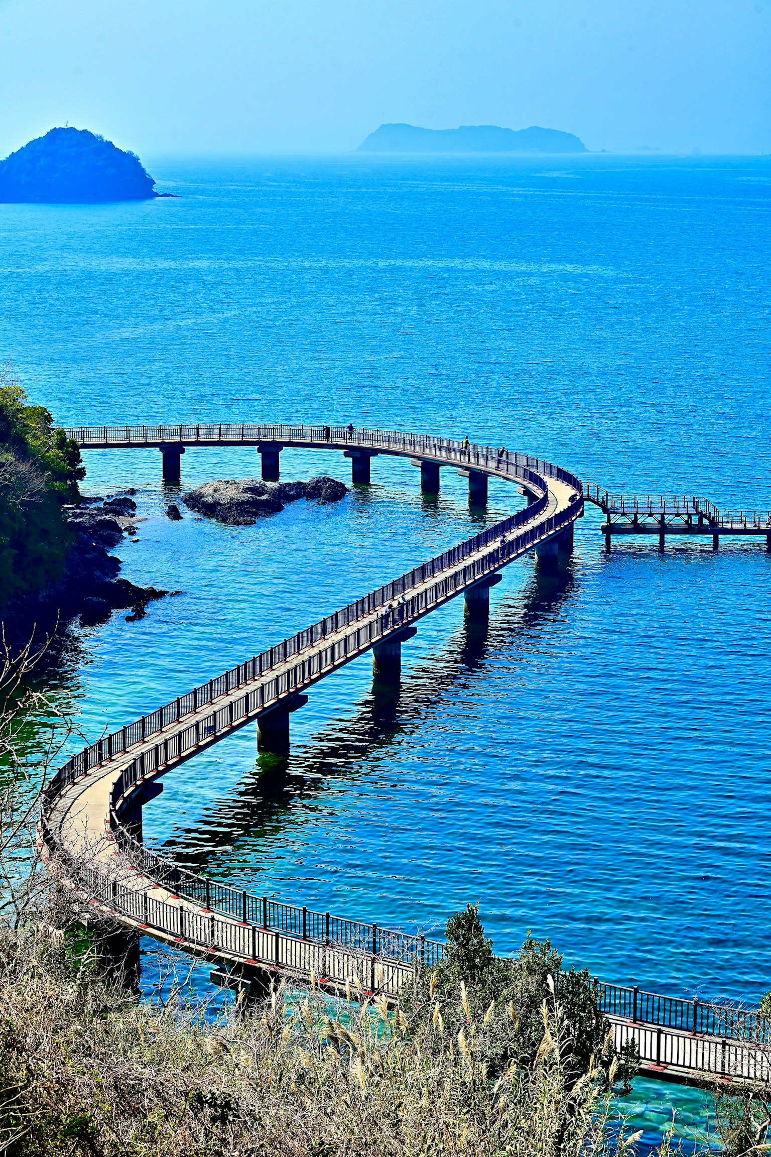 Curved wooden bridge along the blue sea with distant islands