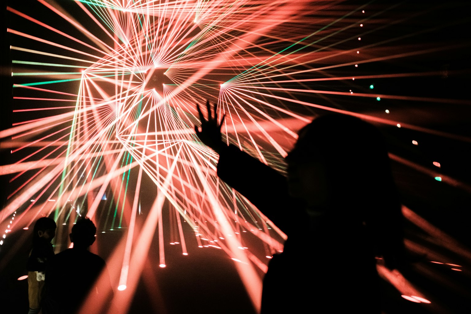 Silhouettes of people raising hands amid colorful intersecting laser beams