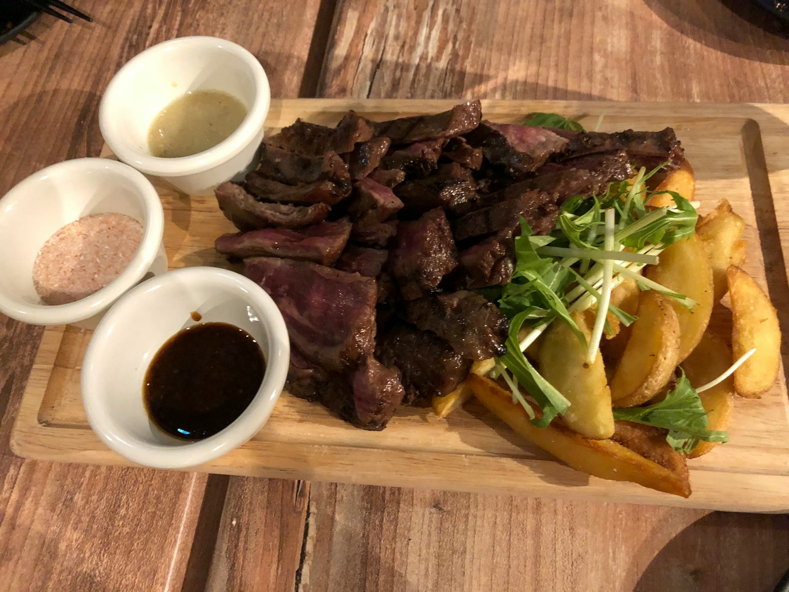 Carne grigliata servita su un tagliere di legno con patatine e salse