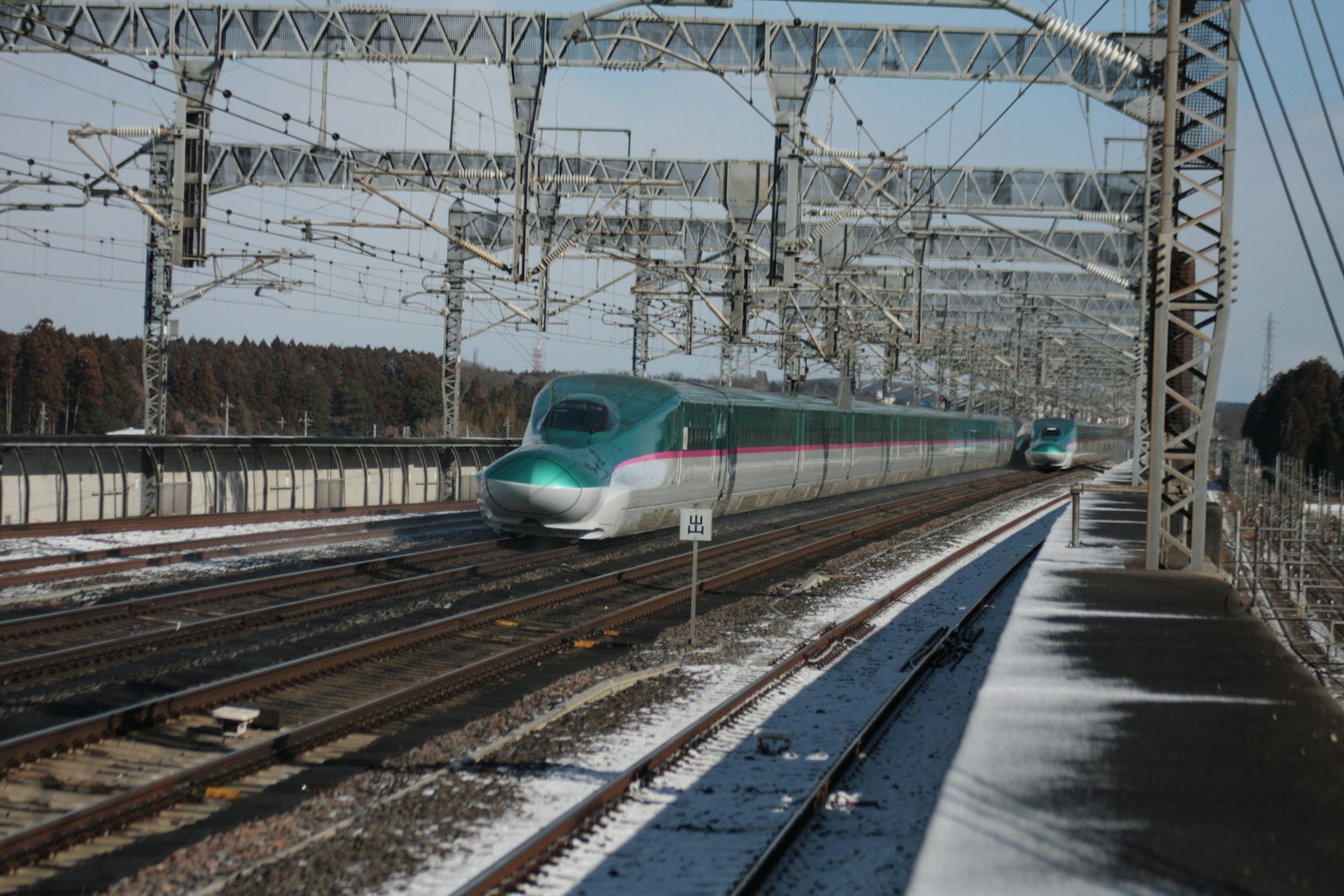 รถไฟชินคันเซ็นวิ่งผ่านภูมิทัศน์ที่มีหิมะพร้อมสายไฟรางรถไฟ