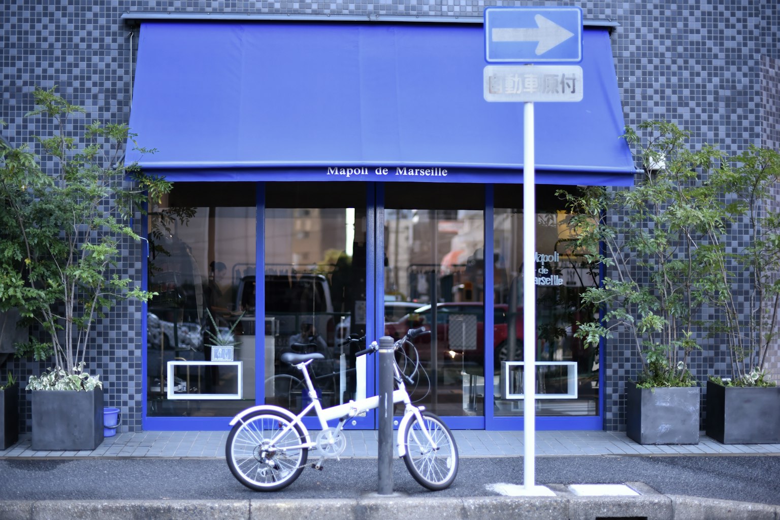 A white bicycle parked in front of a store with a blue awning